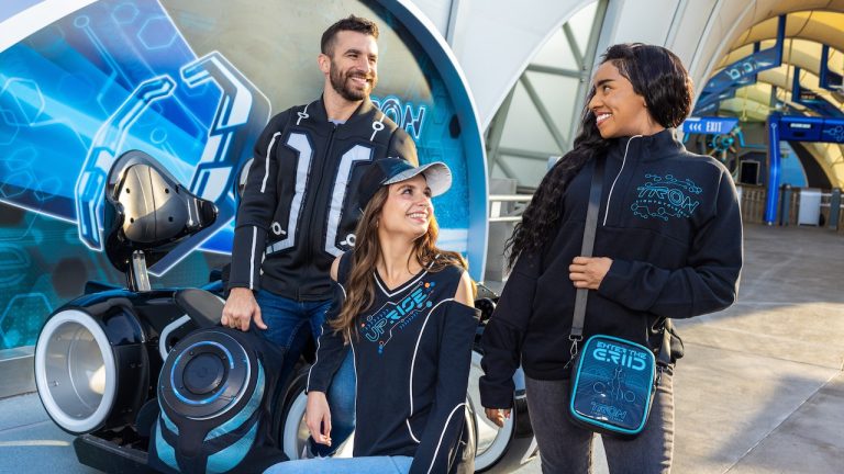 Three people posing in from of the Tron ride wearing tron merchandise