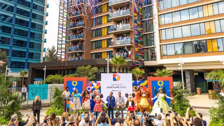 Opening ceremony photo in front of the villas at Disneyland Resort featuring guests, characters, and Disney Cast Members