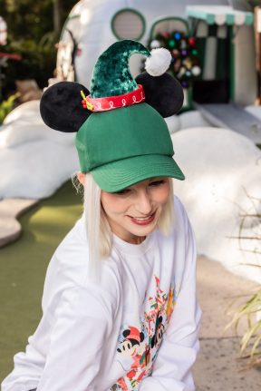 Model wearing conifer-green ballcap topped with a velveteen elf hat and plush Mickey ears