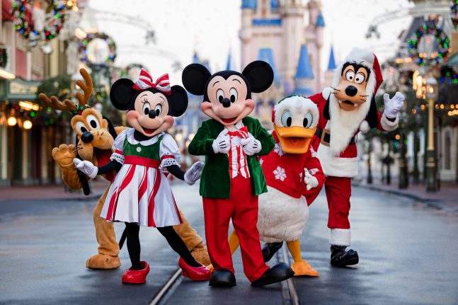 Mickey, Minnie, Donald, Pluto and Goofy pose in holiday attire in front of Cinderella Castle
