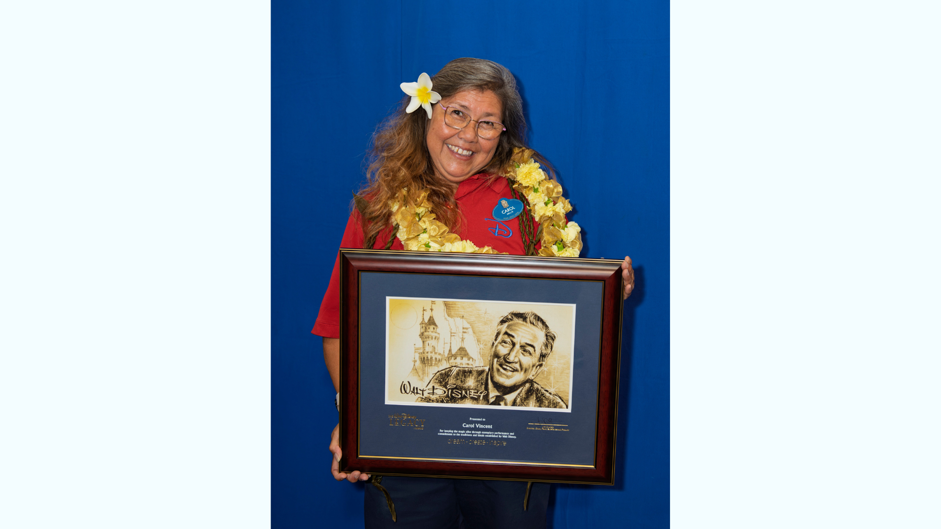 Smiling woman in a floral lei holds a framed award.