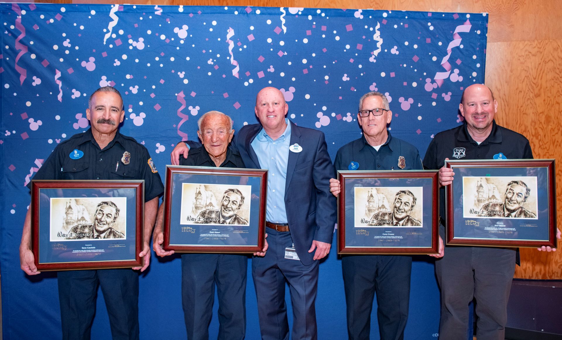 Four individuals holding framed awards in front of a celebratory backdrop.