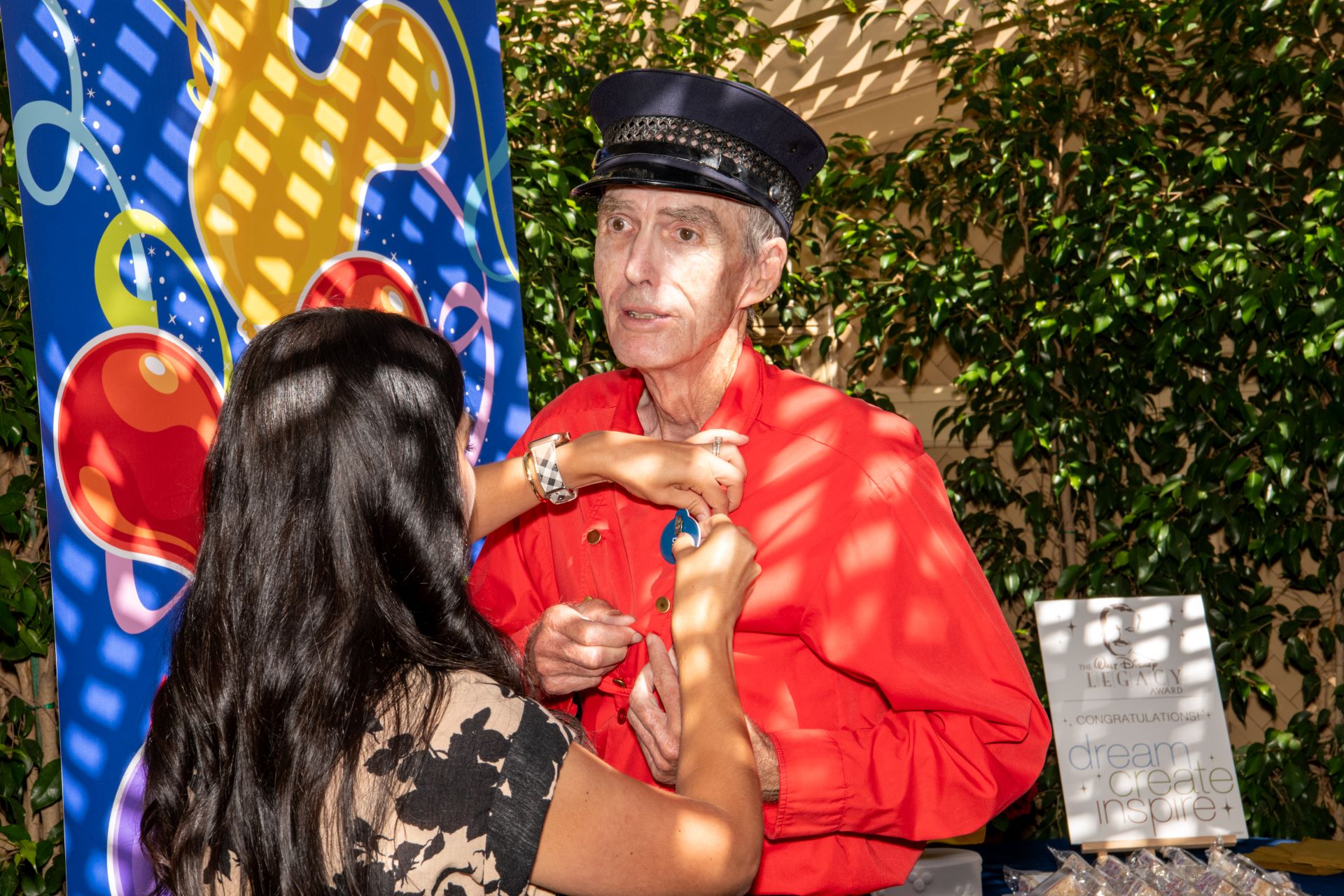 A man in a red shirt receives an award pin from a woman.