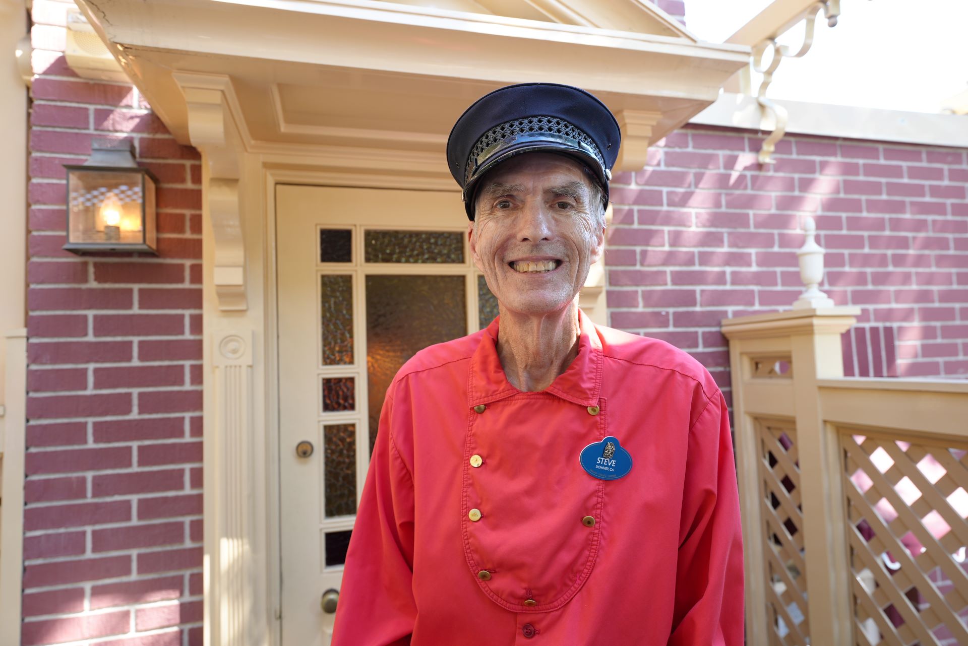 Smiling man in a red uniform stands near a doorway.