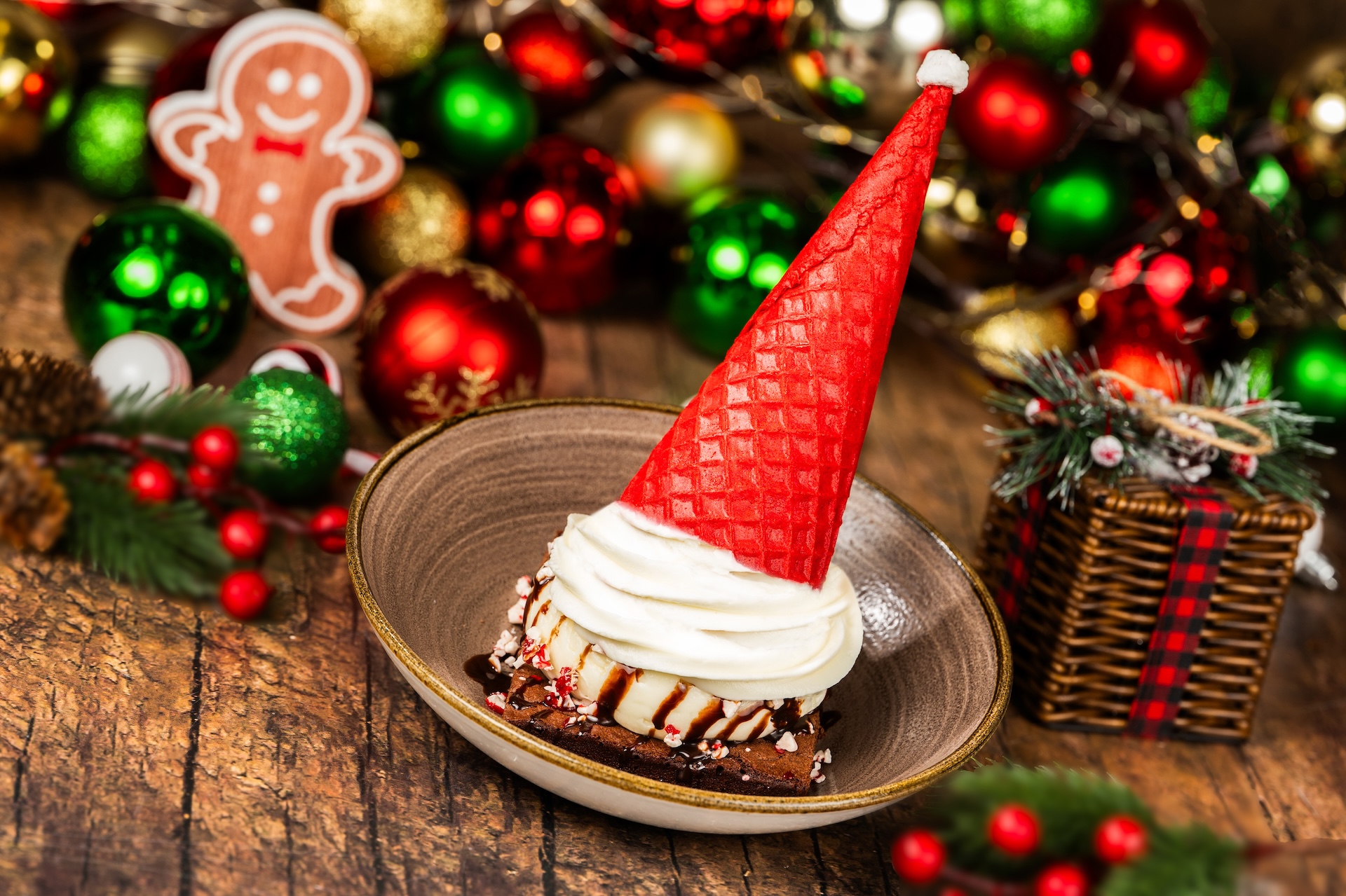 Santa Hat Brownie Sundae: Brownie topped with vanilla ice cream, hot fudge, crushed peppermint, whipped cream, and a red velvet cone with a marshmallow pompom