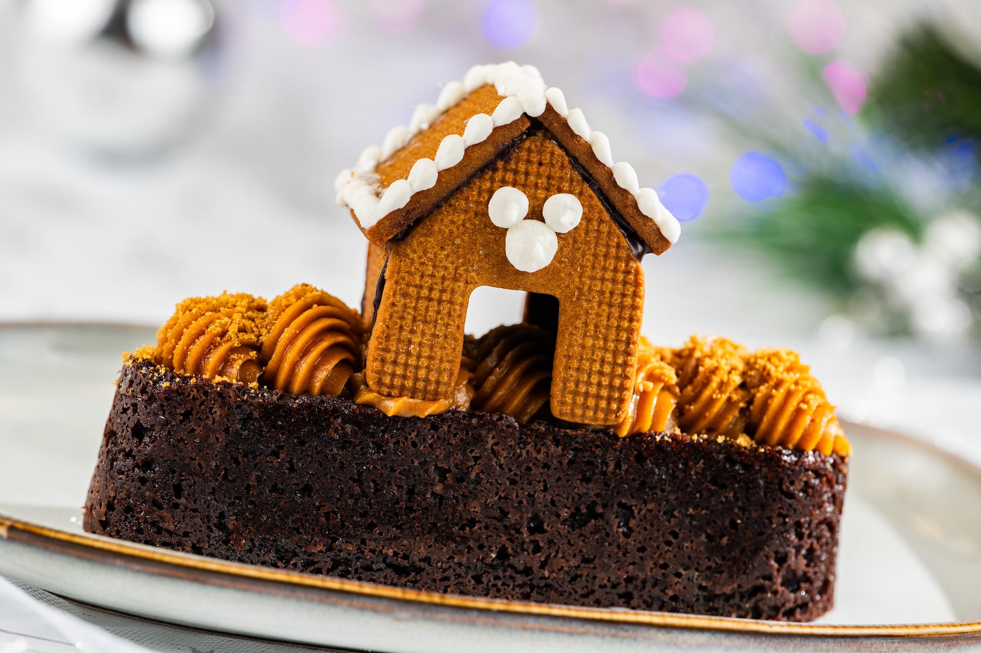 Gingerbread house on a brownie, decorated with frosting and golden swirl.