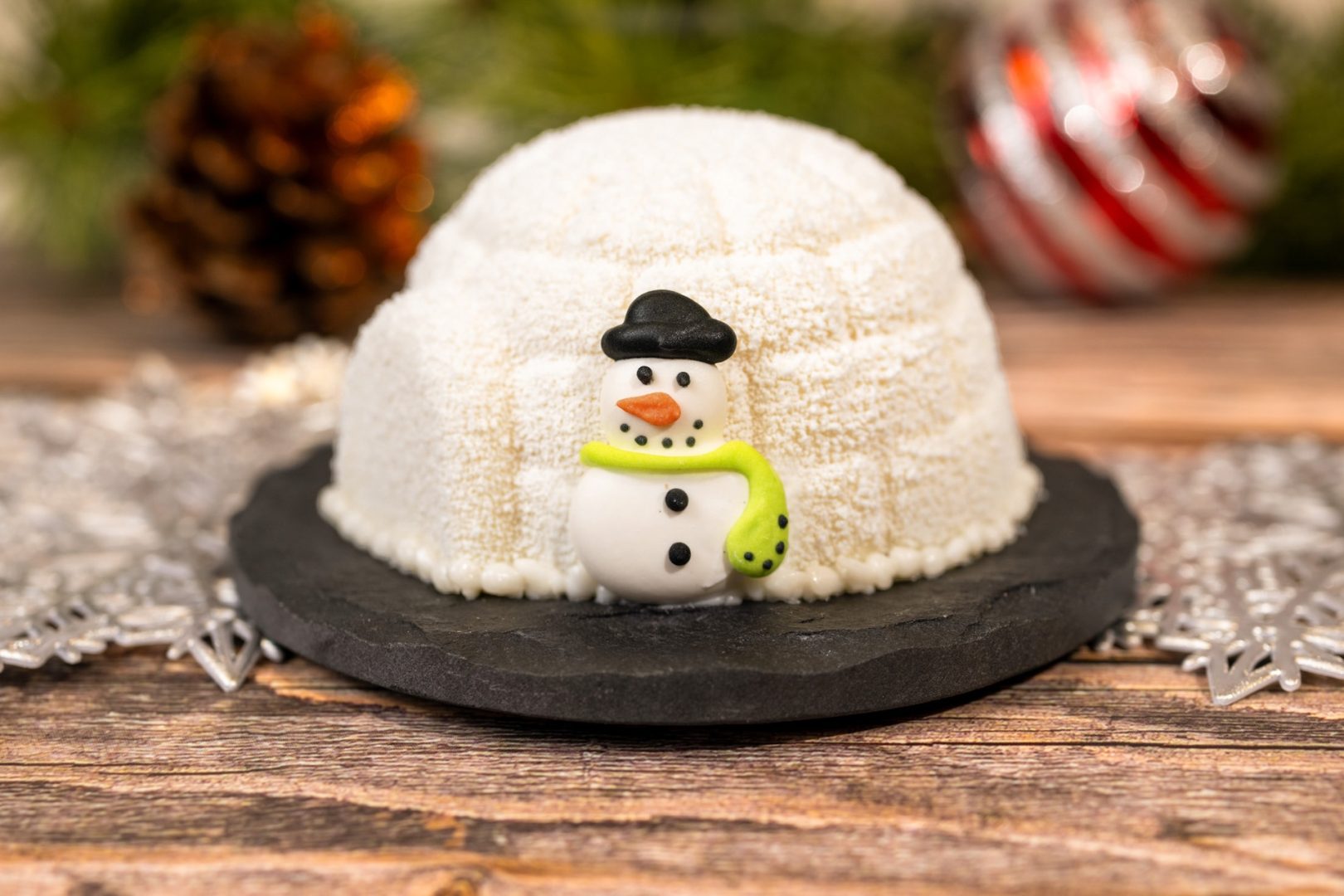 Decorative peppermint igloo dessert with a snowman figurine on a slate plate.