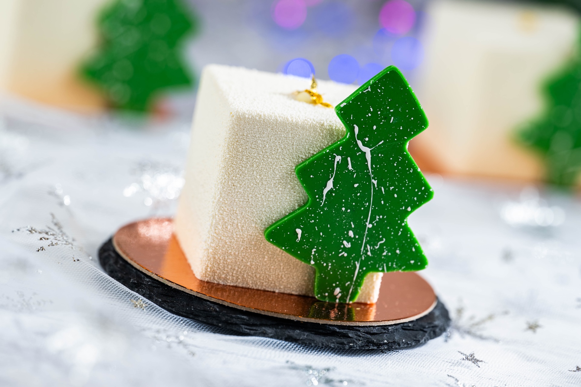Festive dessert featuring a white cube topped with a green tree decoration.