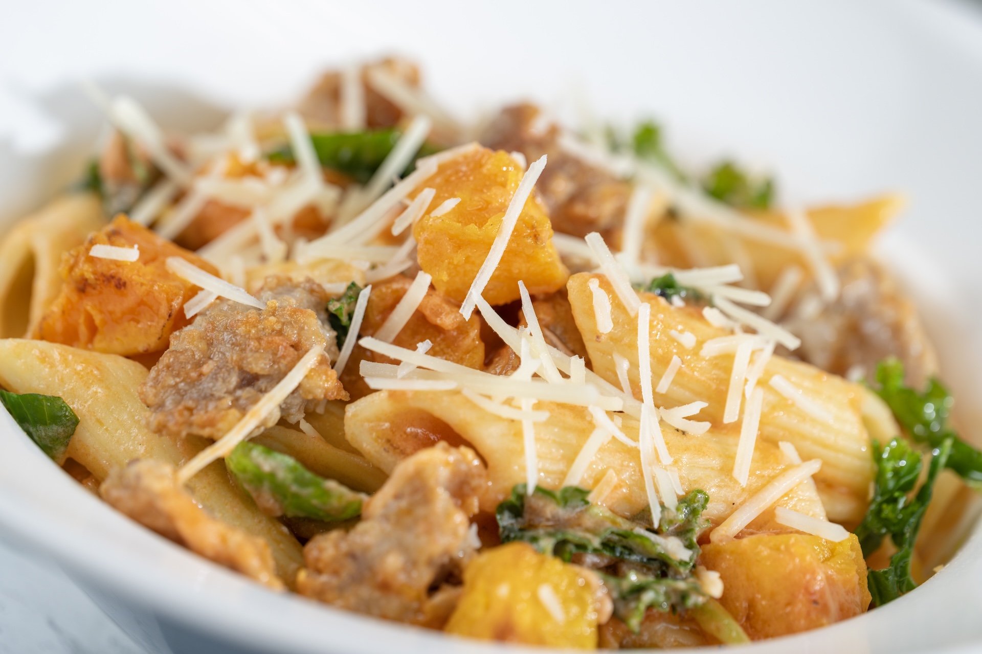 Pasta dish with squash, sausage, and garnished with shredded cheese.