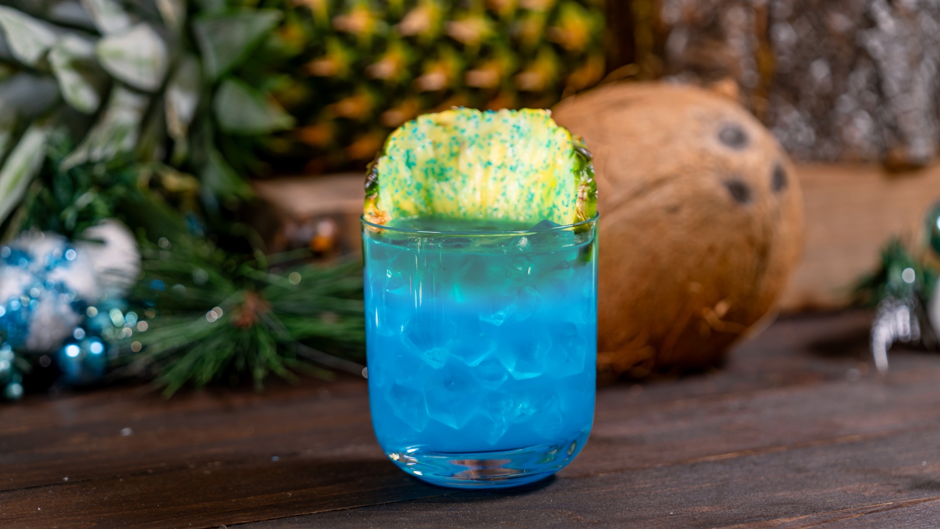 Blue Tropical Cocktail: Rum, pineapple, orange and lemon juices, blue raspberry syrup, and coconut purée garnished with a blue sugar-coated pineapple wheel and a dark rum float