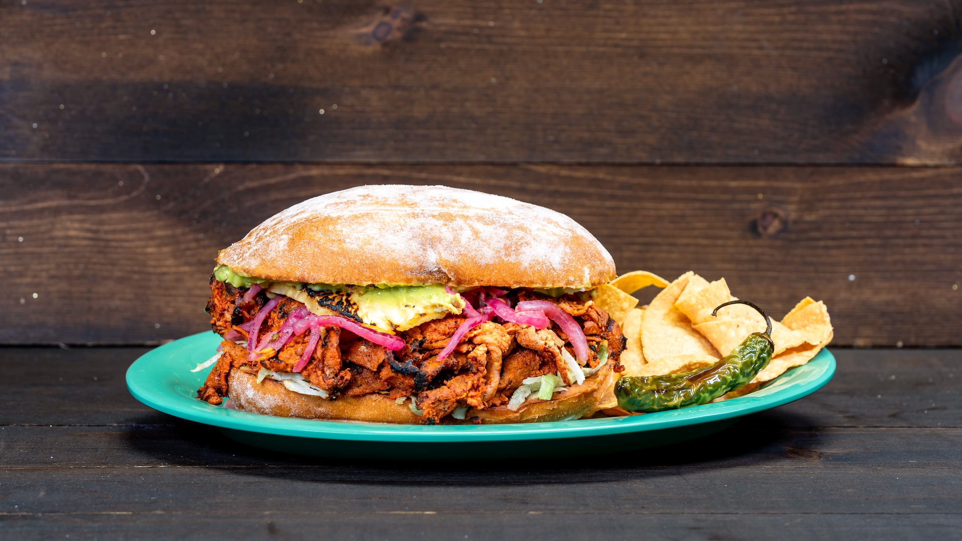 Al Pastor Torta: Pineapple achiote-marinated pork with chorizo beans, avocado spread, tomatillo salsa, cilantro, and onions served with tortilla chips (New)