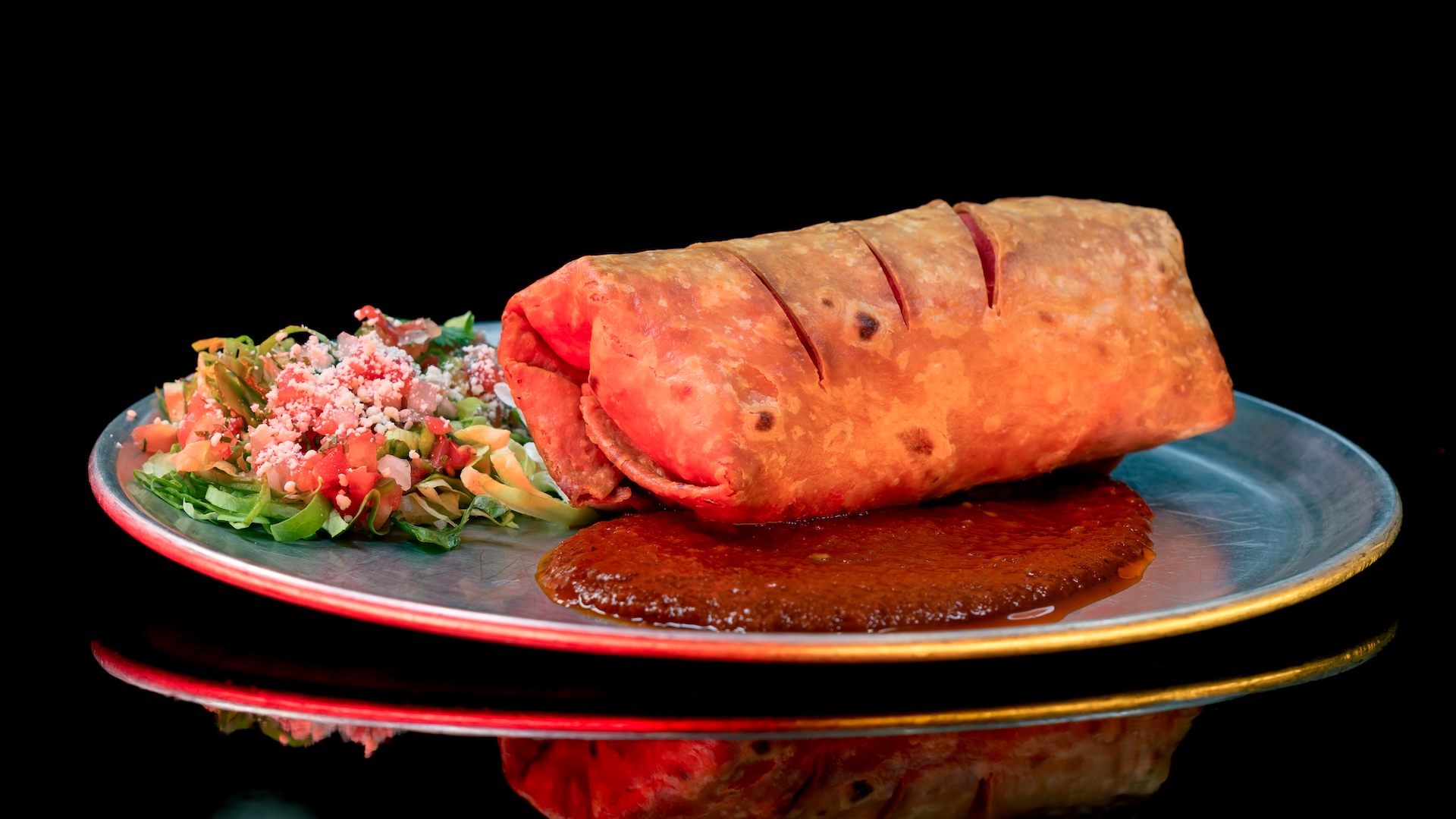 The Chimichanga with seasoned beef, charred poblano, refried beans, and shredded cheese, on a pool of guajillo sauce with a pico de gallo side salad