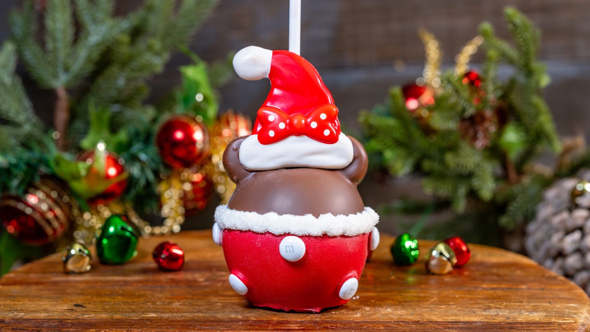 Santa Minnie Caramel Apple: Green apple dipped in caramel with two marshmallow ears, dipped in milk chocolate, and decorated with red-colored white chocolate, white sanding sugar, white M&M’S Milk Chocolate Candies, and a white chocolate Santa hat with a bow (New) 
