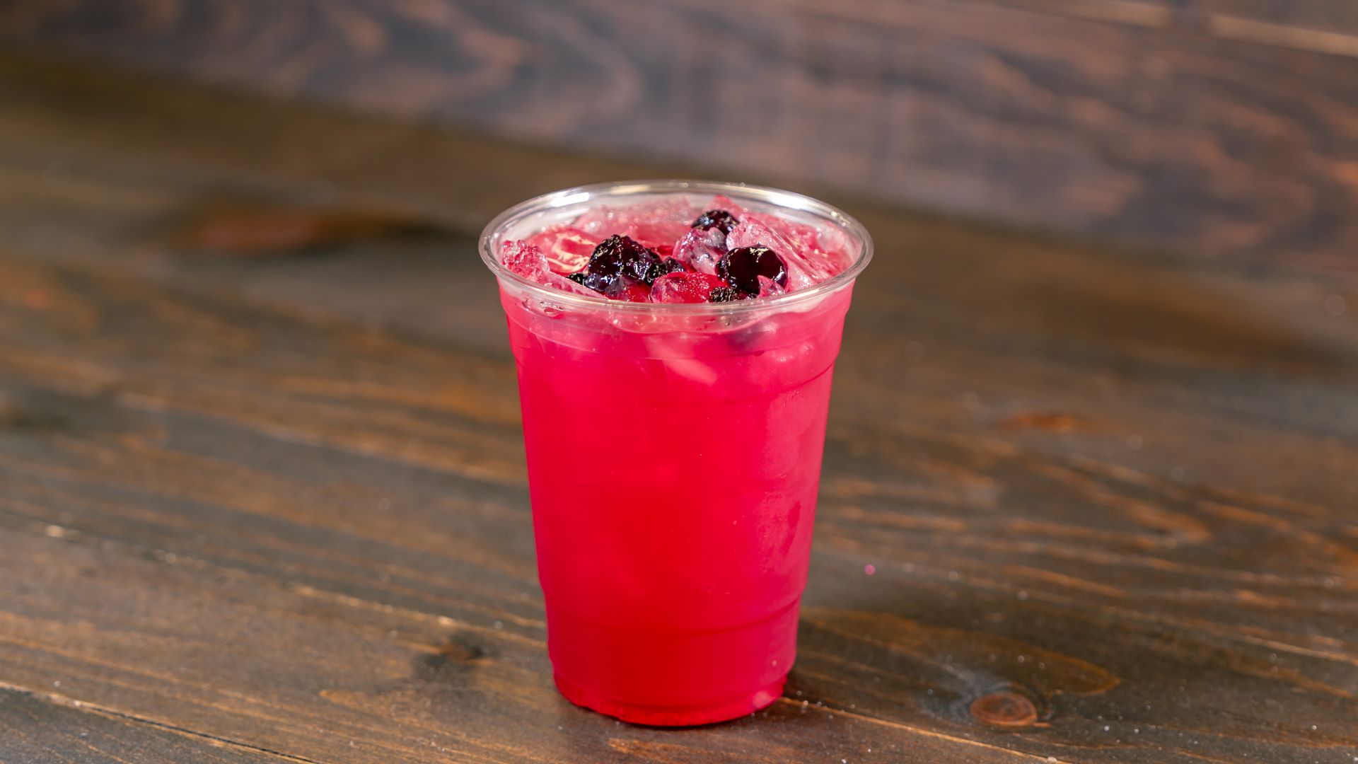 Bright pink drink with ice and blackberries in a clear cup.