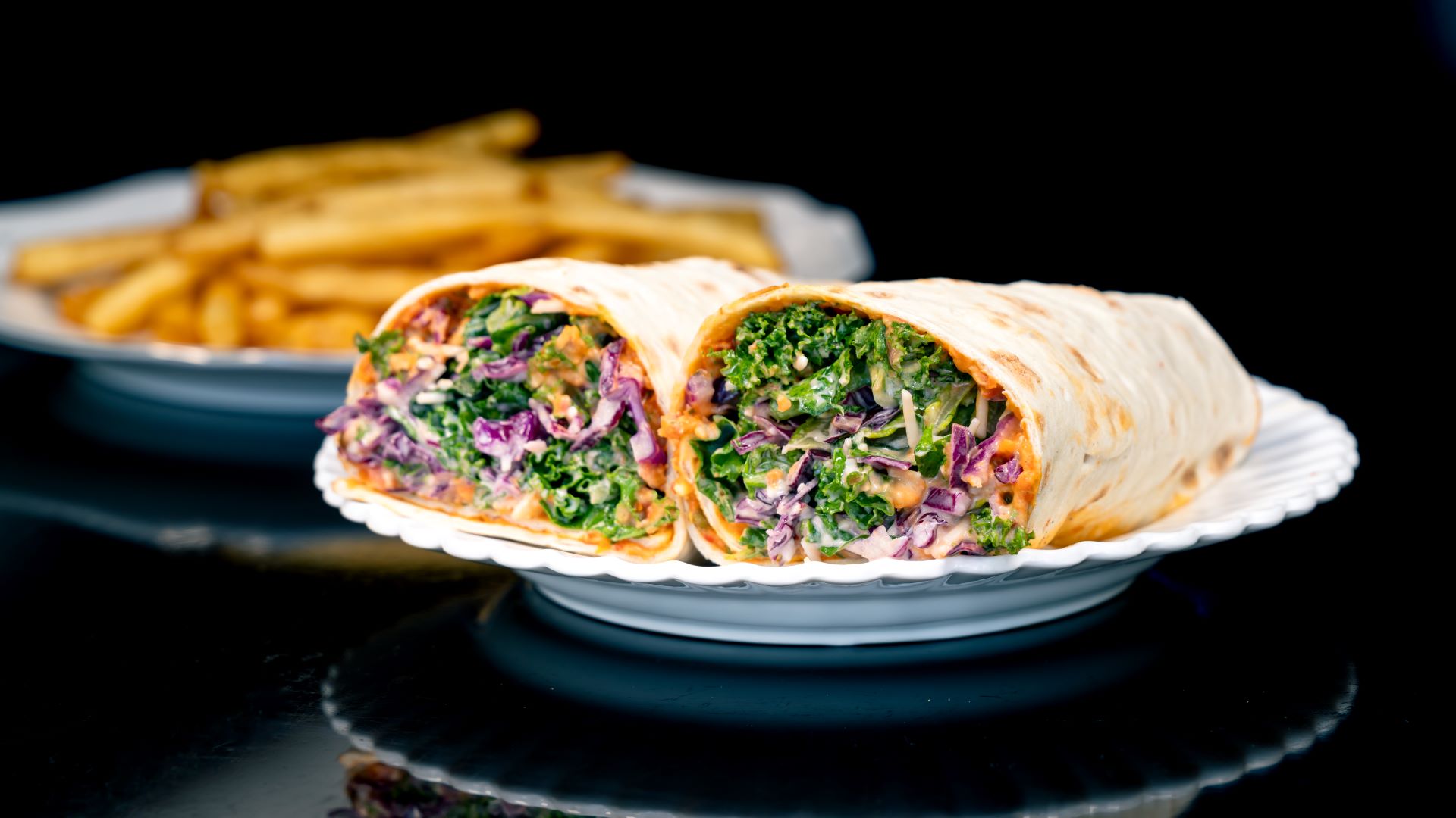 Two garden wraps filled with greens on a plate, with fries in the background.