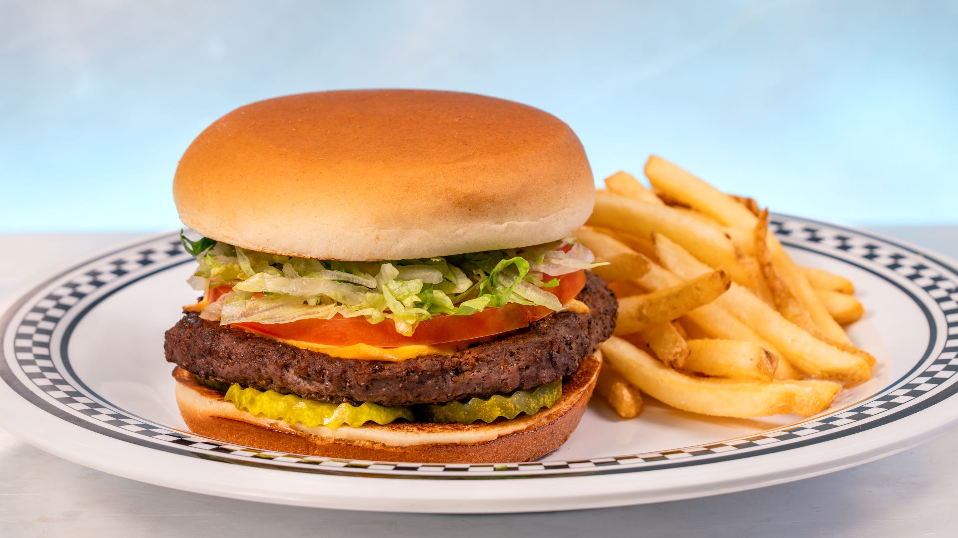 Cheeseburger with lettuce, tomato, and fries on a plate.