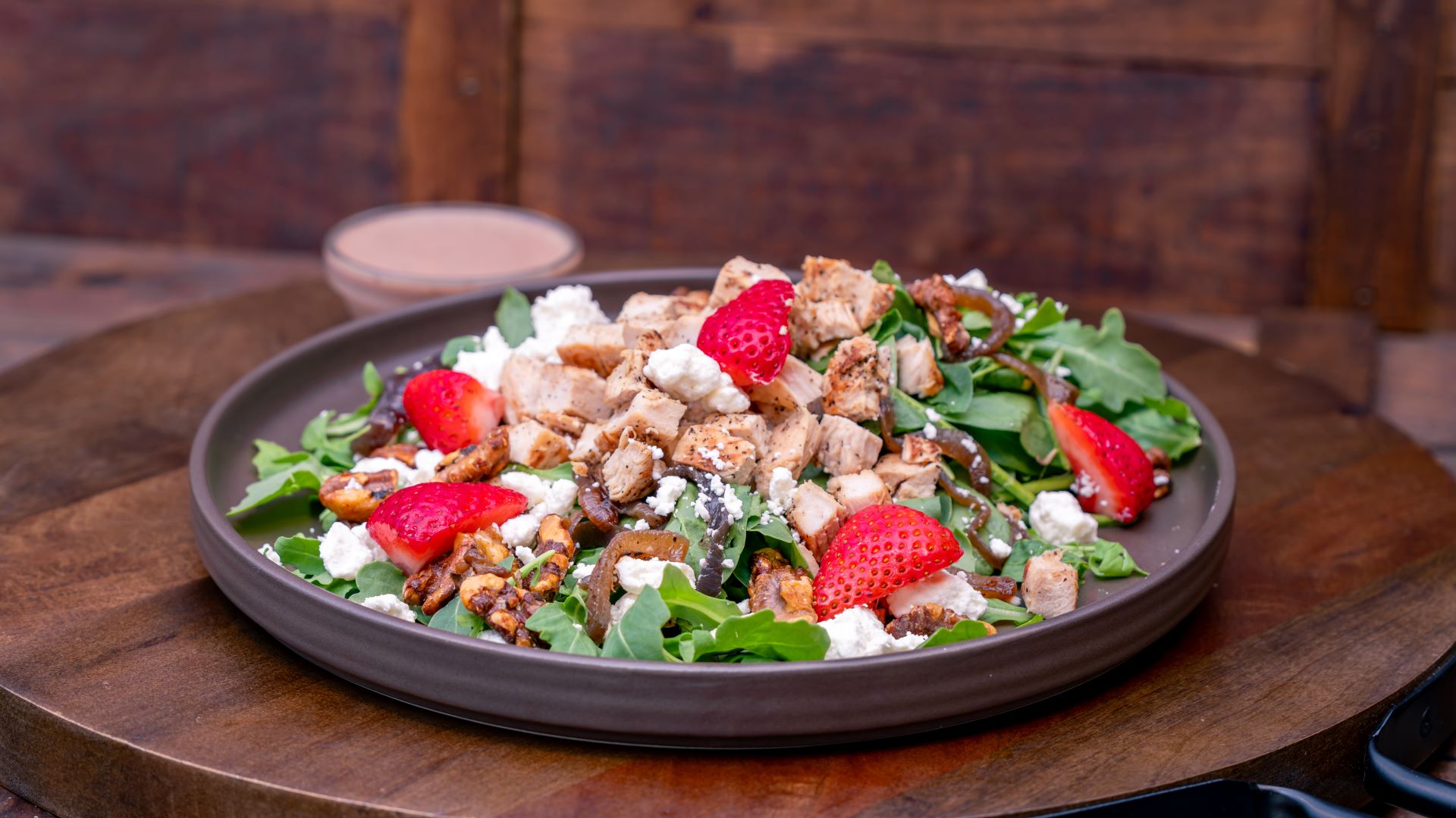 Grilled chicken salad with strawberries, feta, and mixed greens on a plate.
