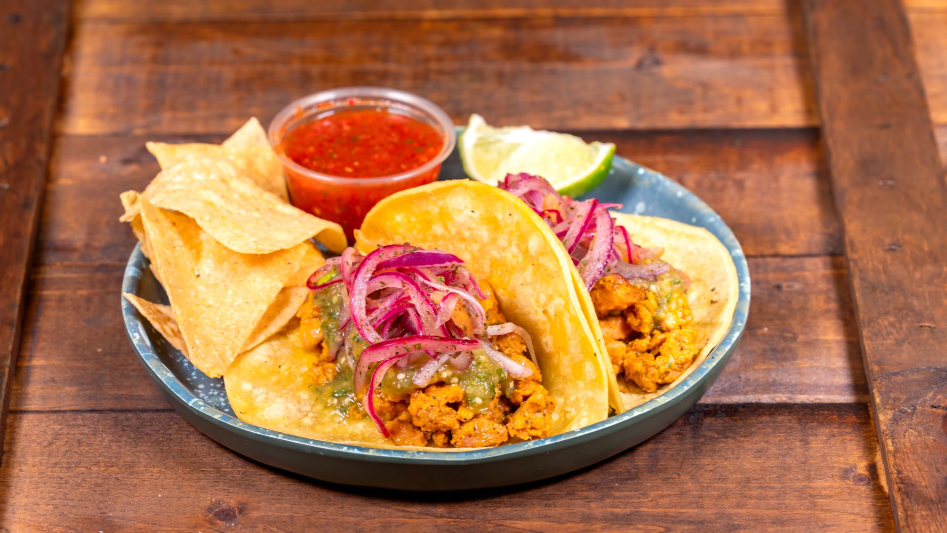 Two chicken tacos topped with onions, served with chips and salsa.