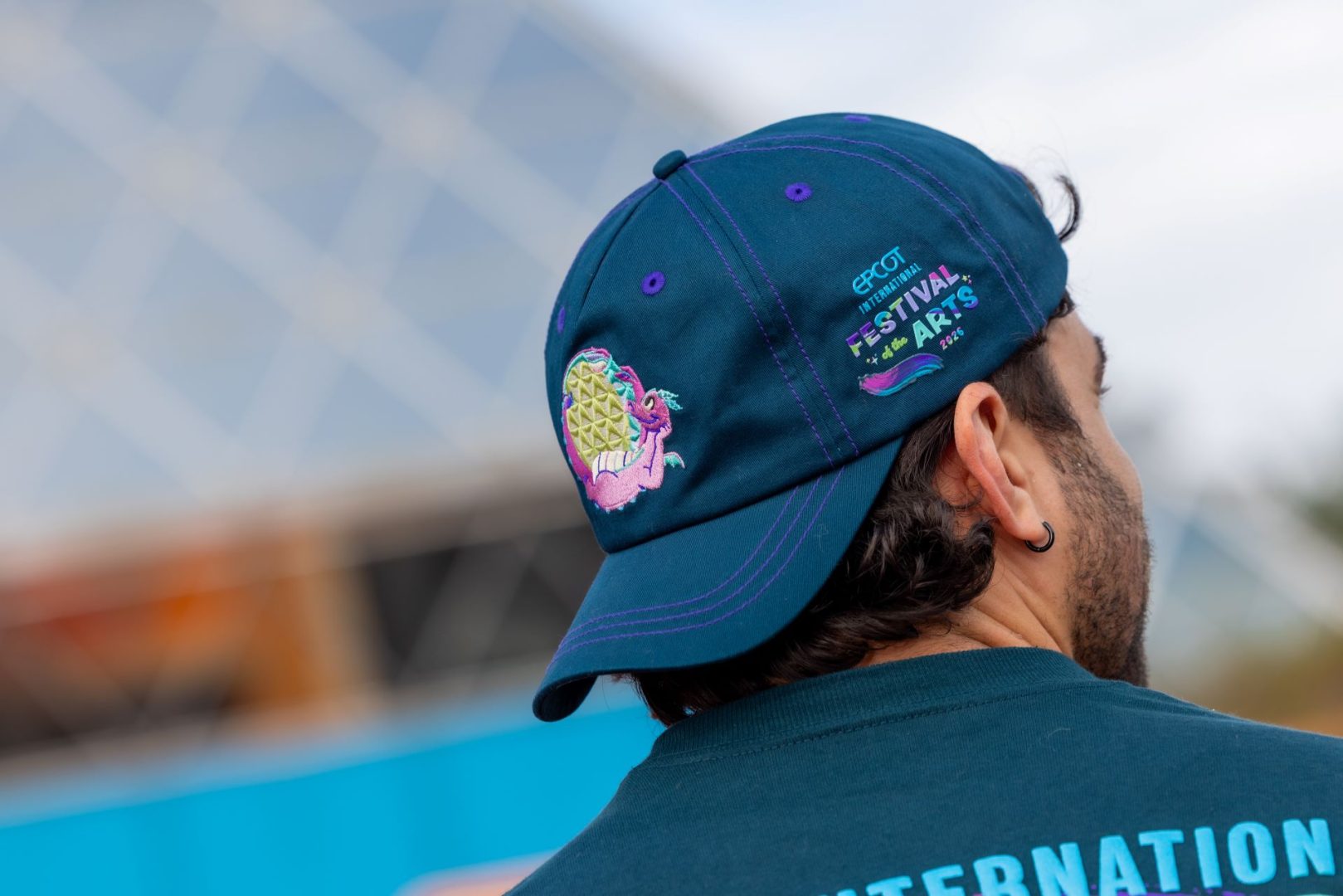 Person wearing a blue baseball hat featuring colorful Festival of the Arts artwork.