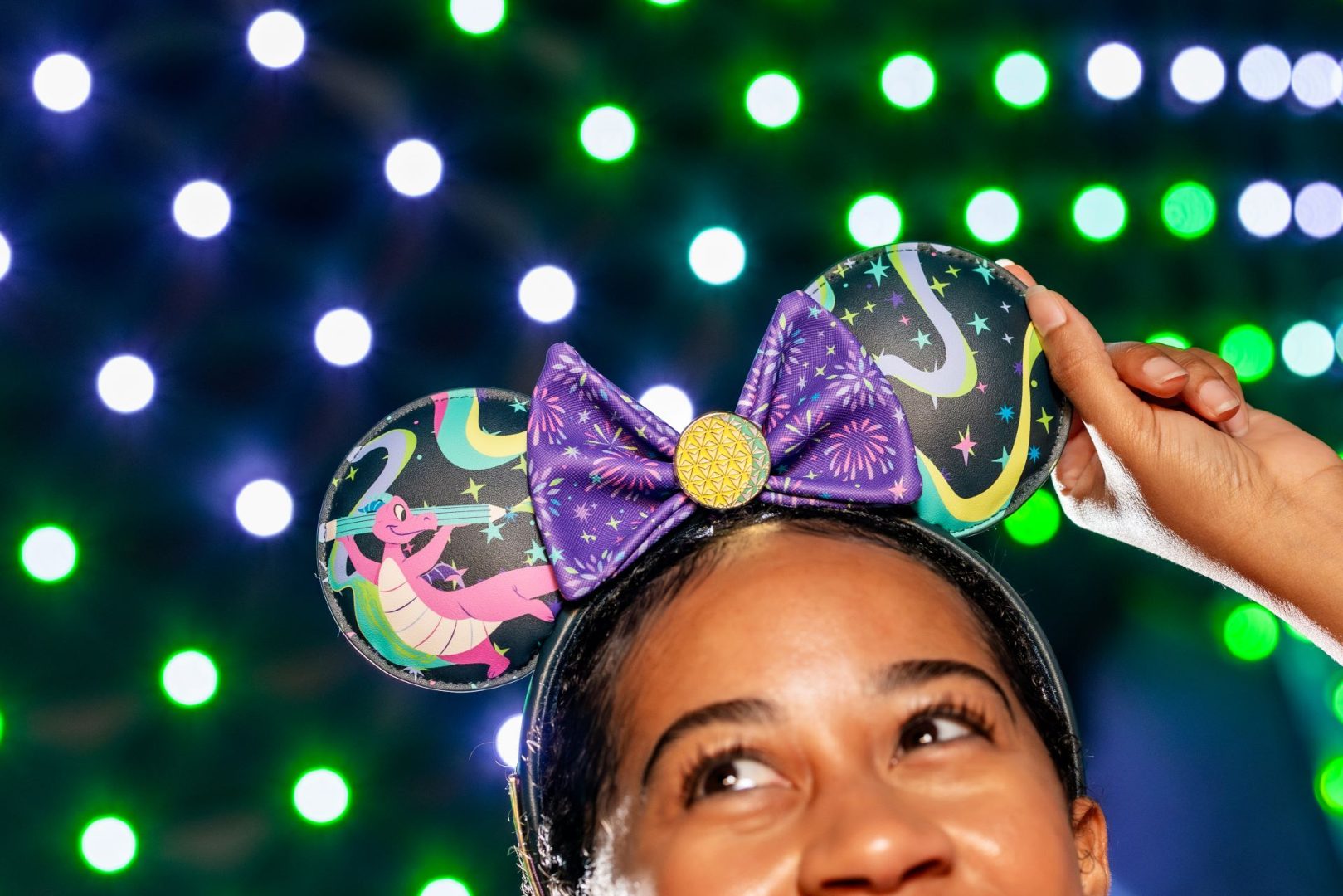 A woman holds Disney ear headband with colorful designs and a purple bow.