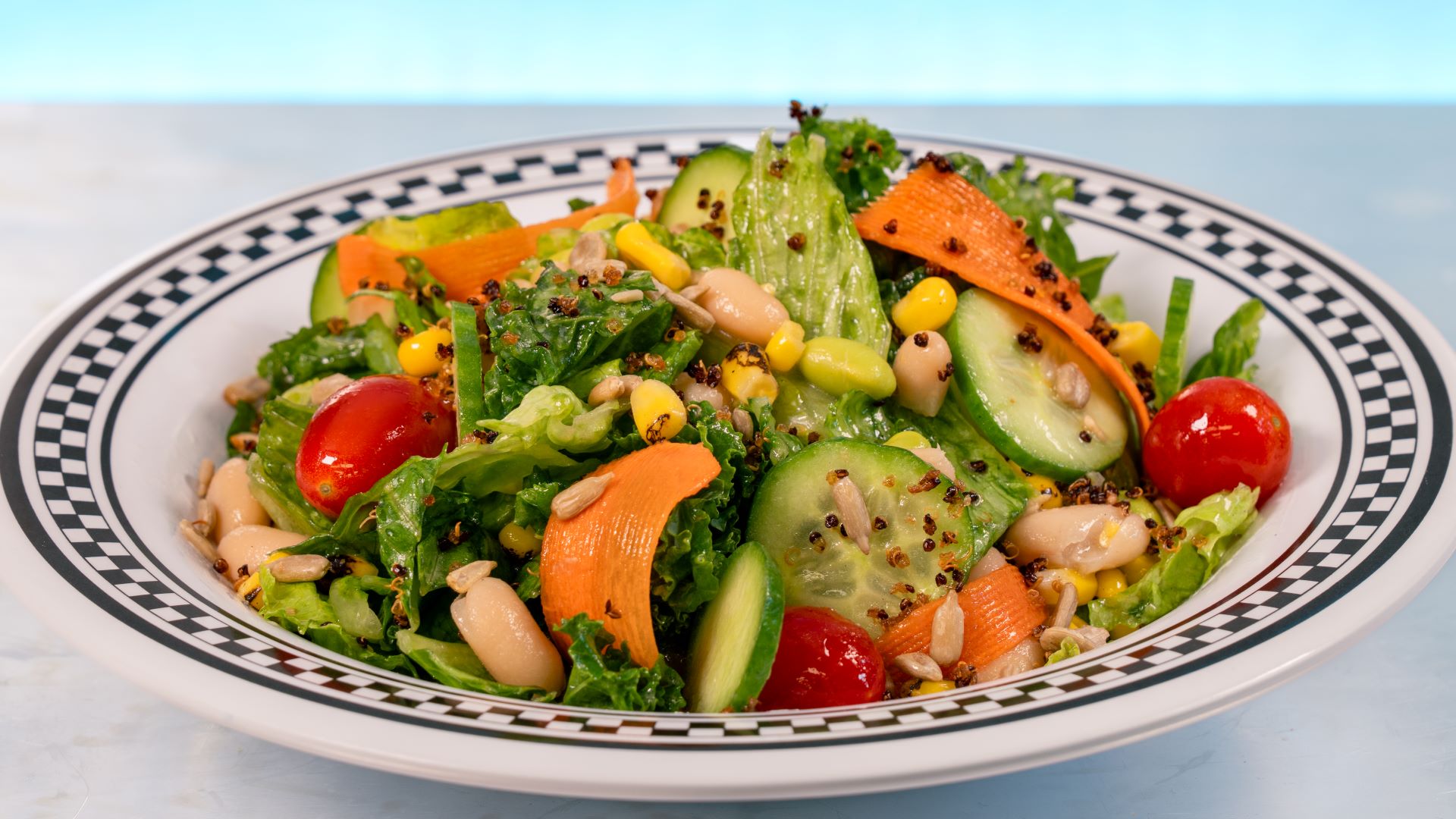 Colorful salad with lettuce, tomatoes, cucumber, corn, and carrots in a bowl.