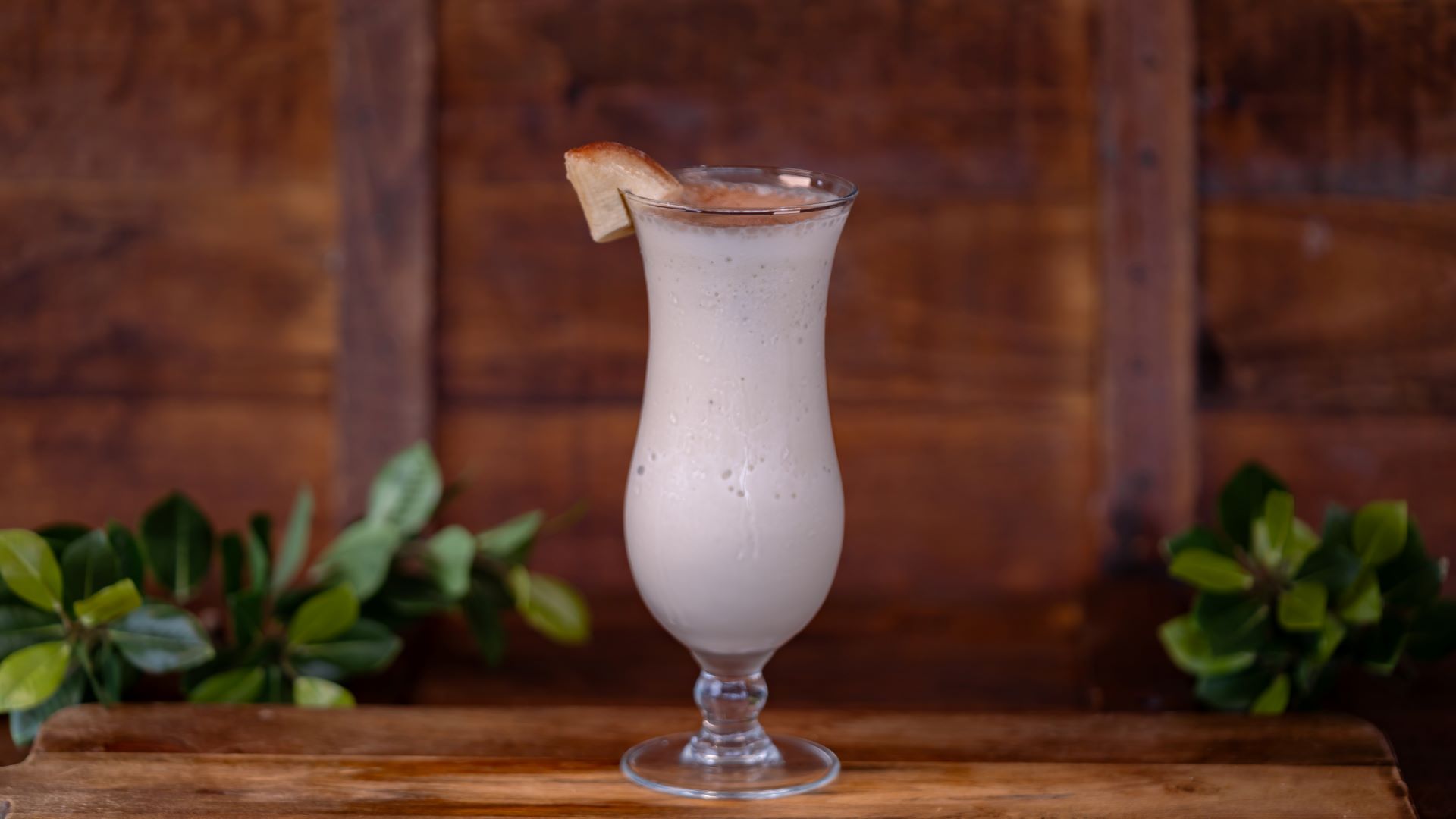 A glass of banana cream cocktail garnished with banana slice.