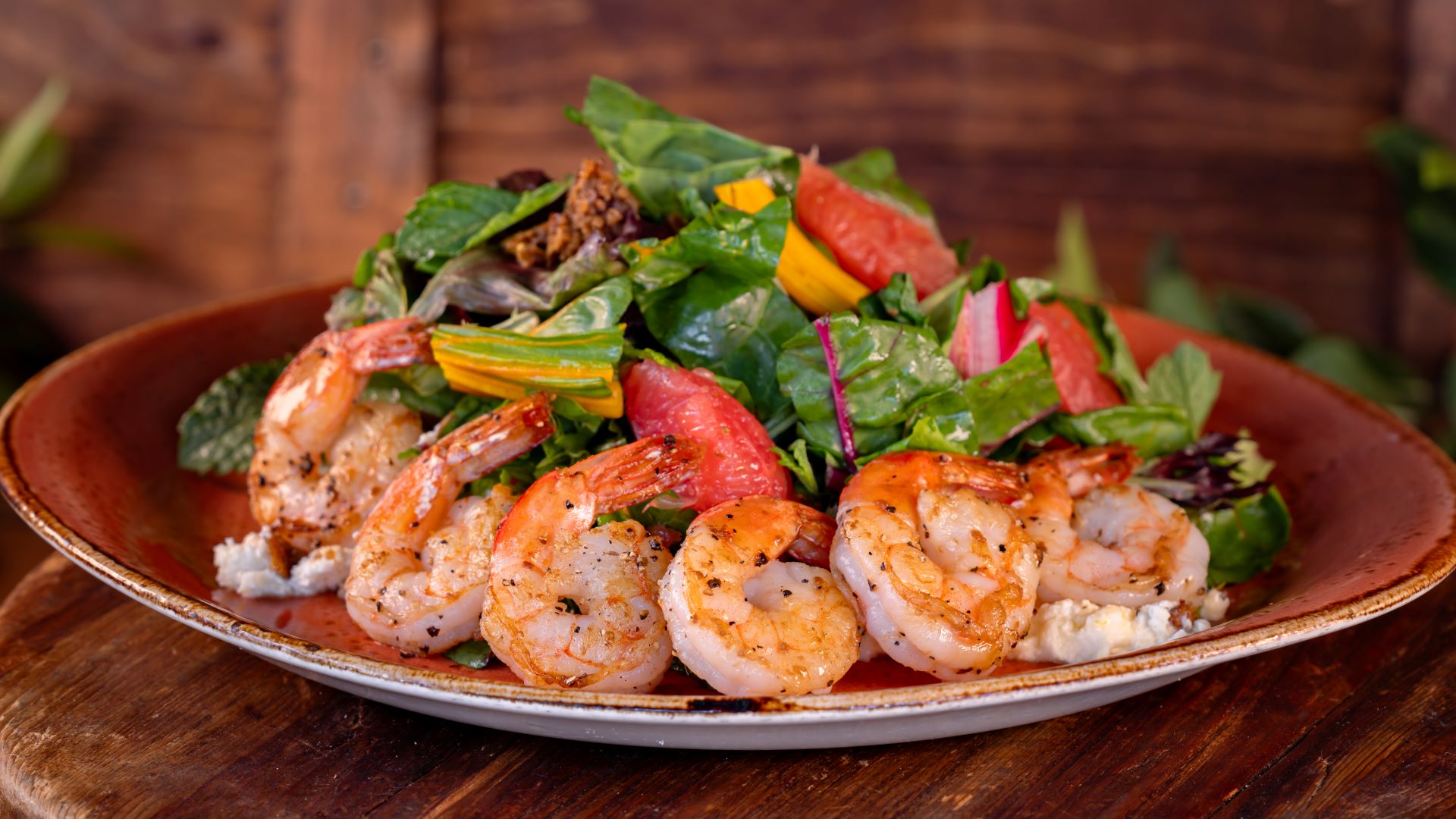 Grilled shrimp atop a vibrant salad with greens and citrus fruits.