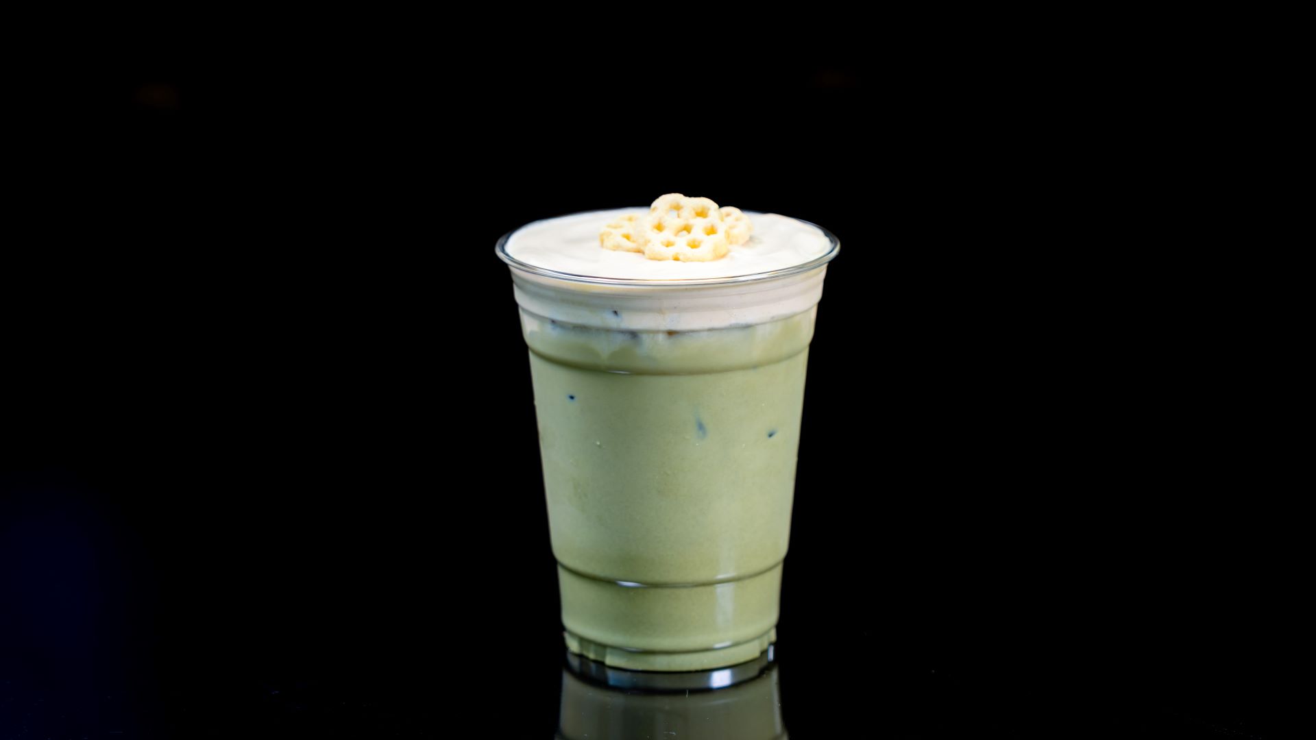 Iced honey matcha tea topped with whipped cream and decorative honeycomb.