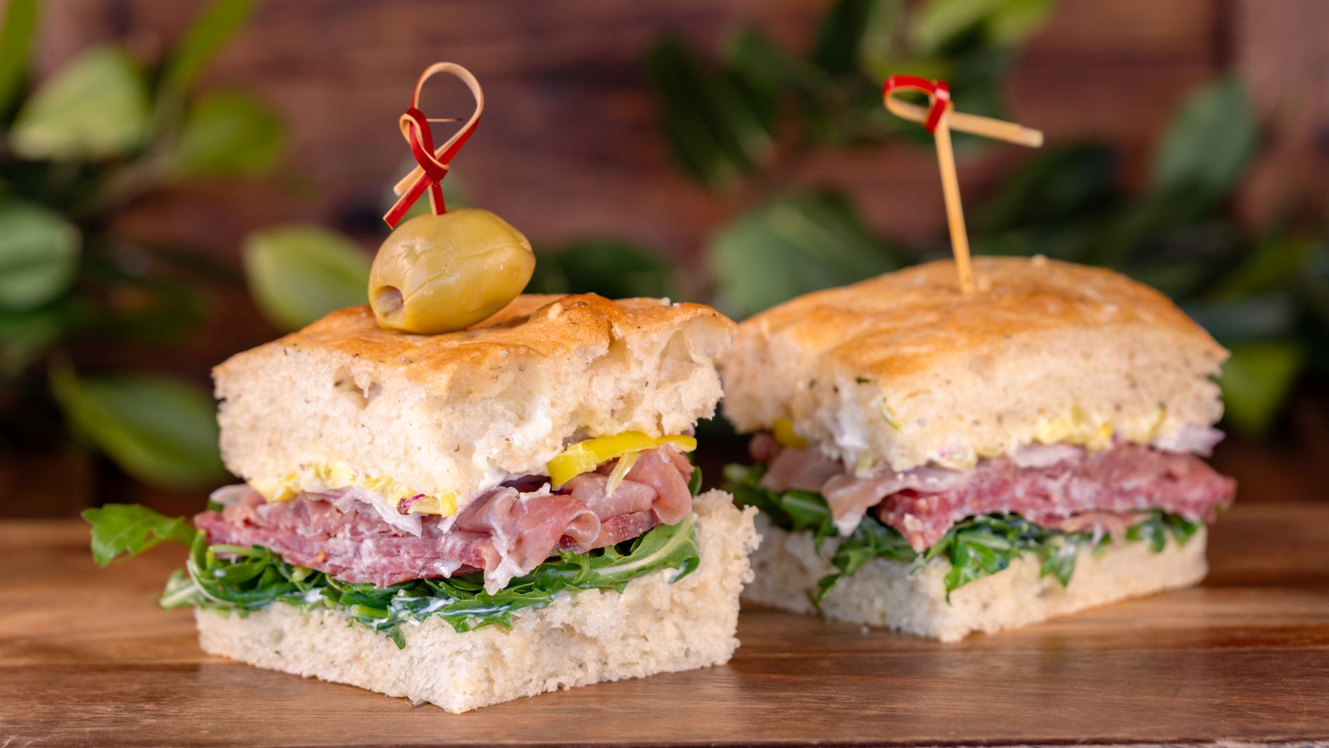 Italian sandwich with deli meats and greens, garnished with an olive.