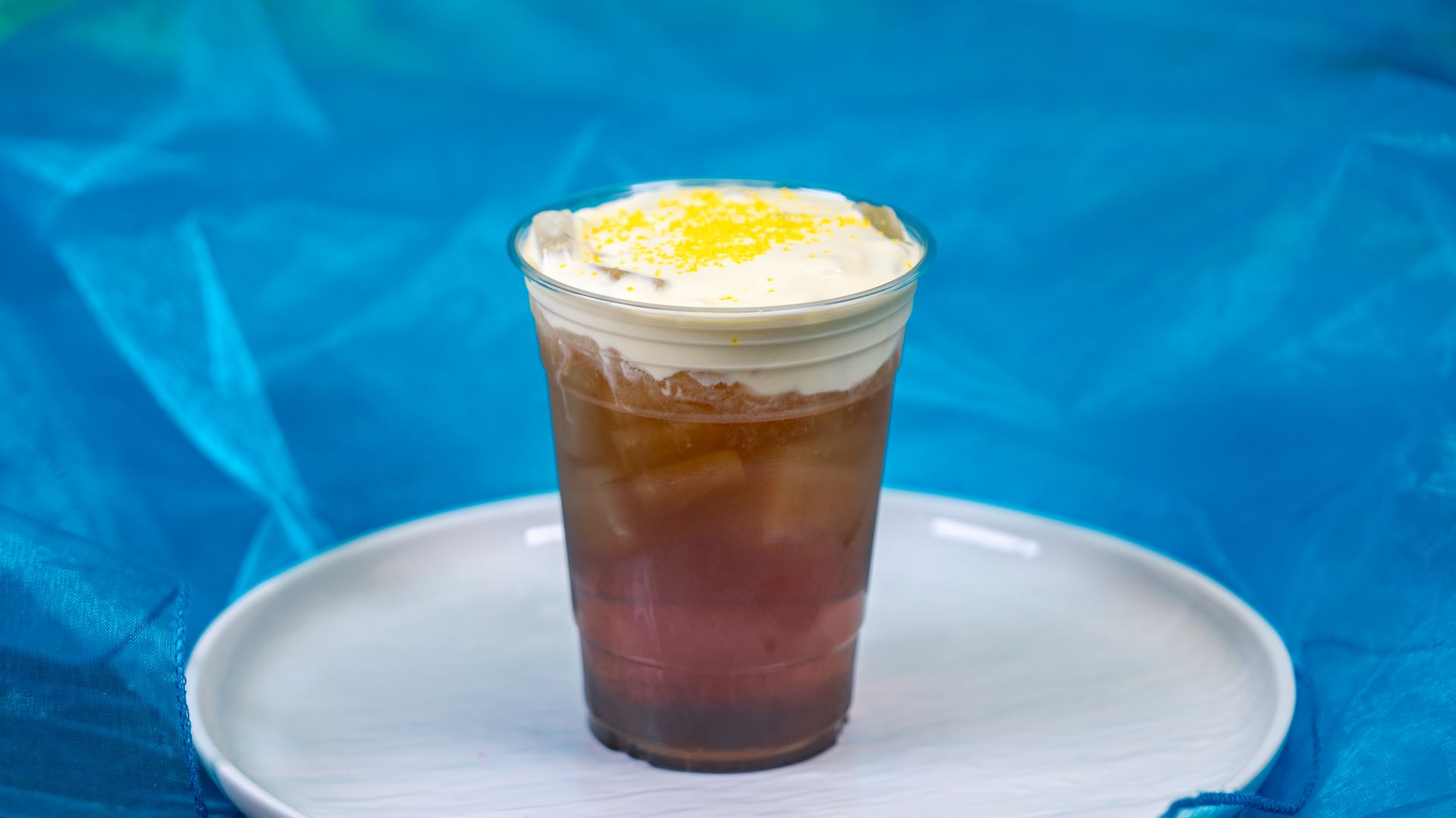 Iced tea layered with cream and yellow sprinkles, served in a clear cup.