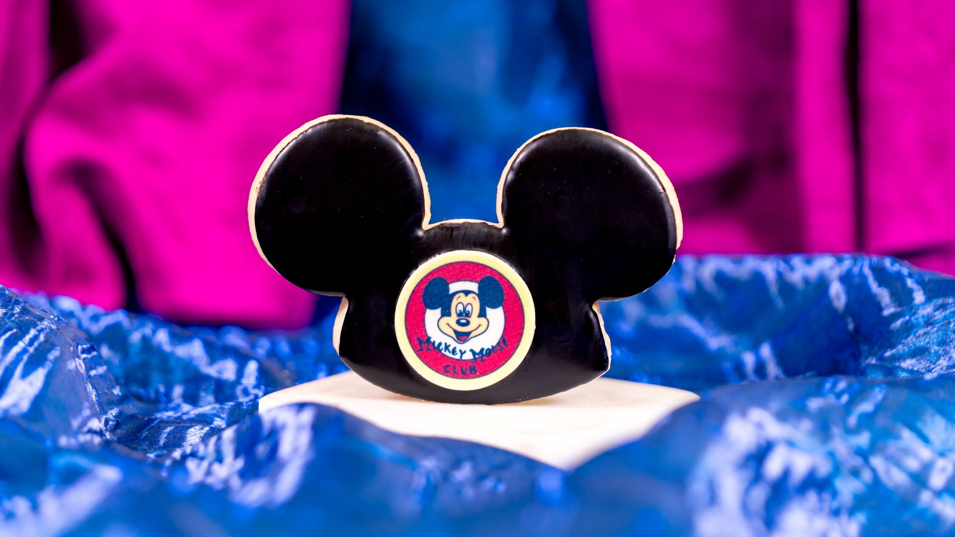Mickey Mouse-shaped cookie decorated with a colorful logo on a blue background.