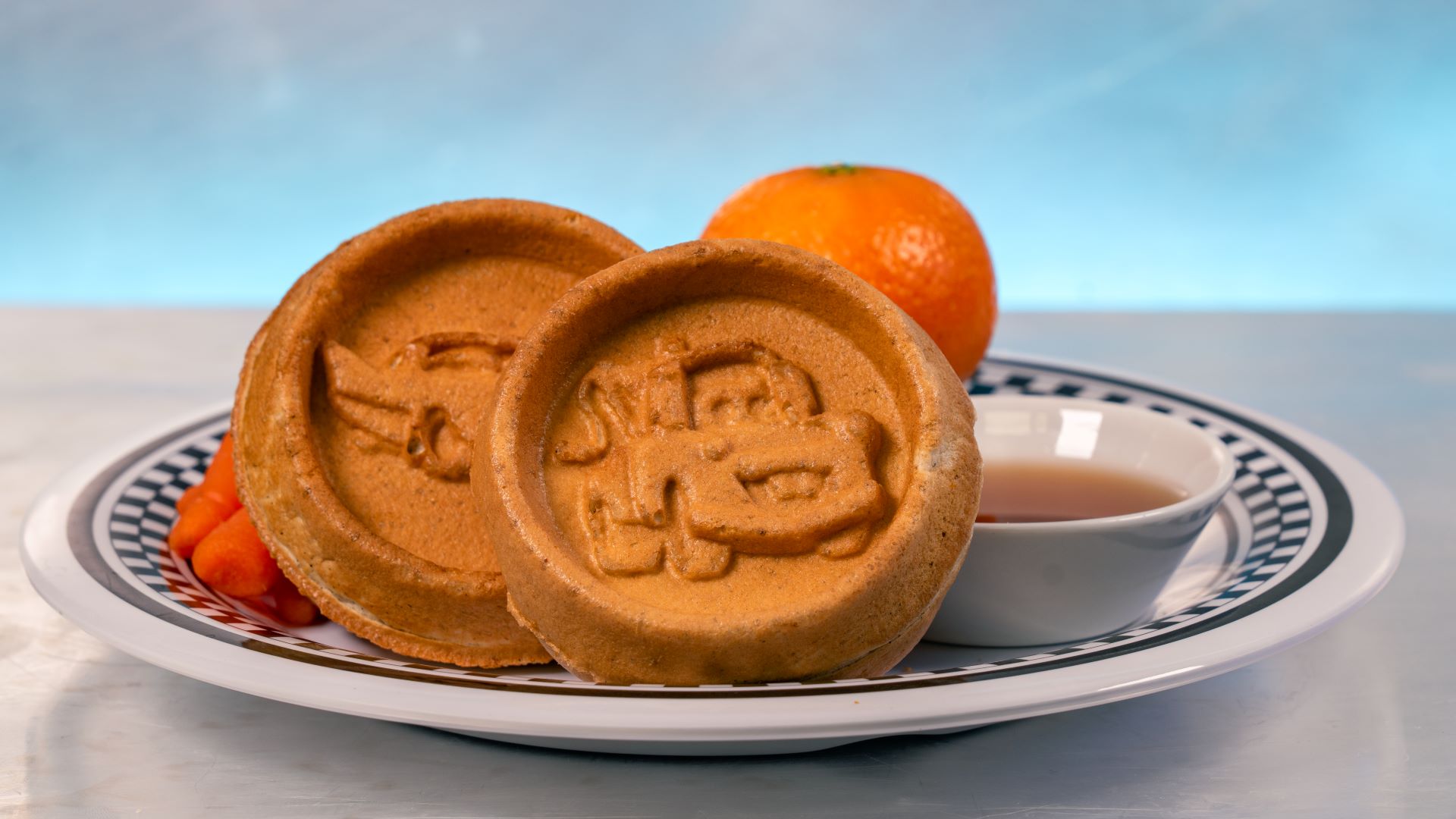 Mini waffles shaped like cars, served with syrup and an orange.