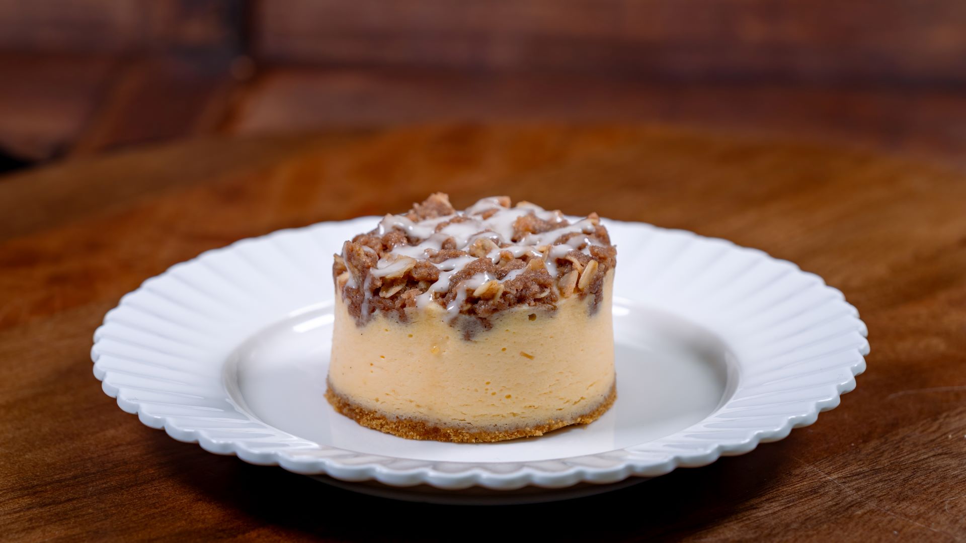 Peach cobbler cheesecake on a white plate, set on a wooden table.