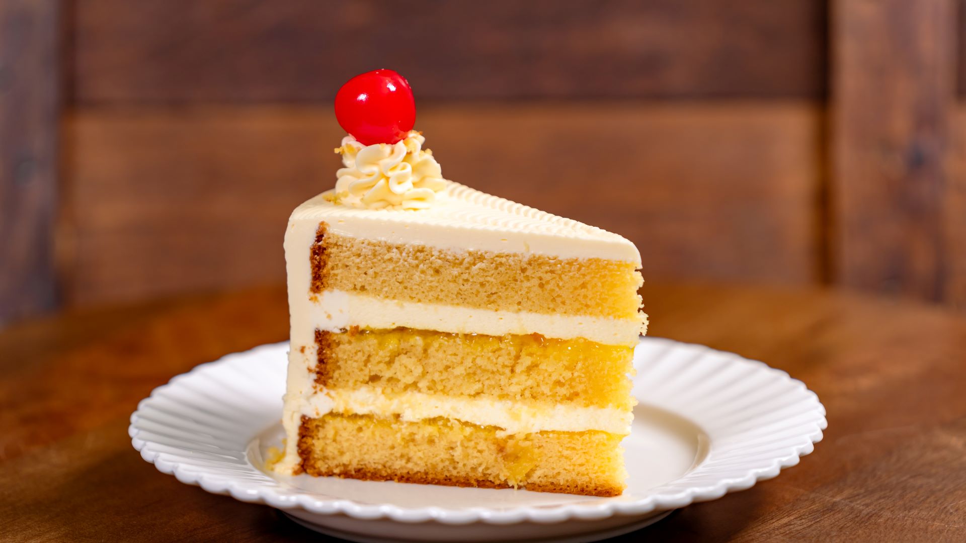 Slice of pineapple upside-down cake topped with cream and cherries on a plate.
