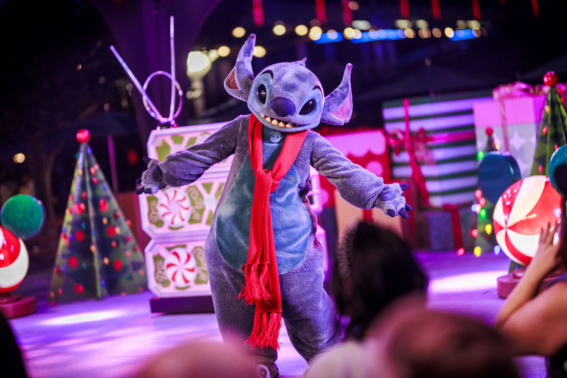 Stitch in a red scarf performing at Disneyland holiday event.