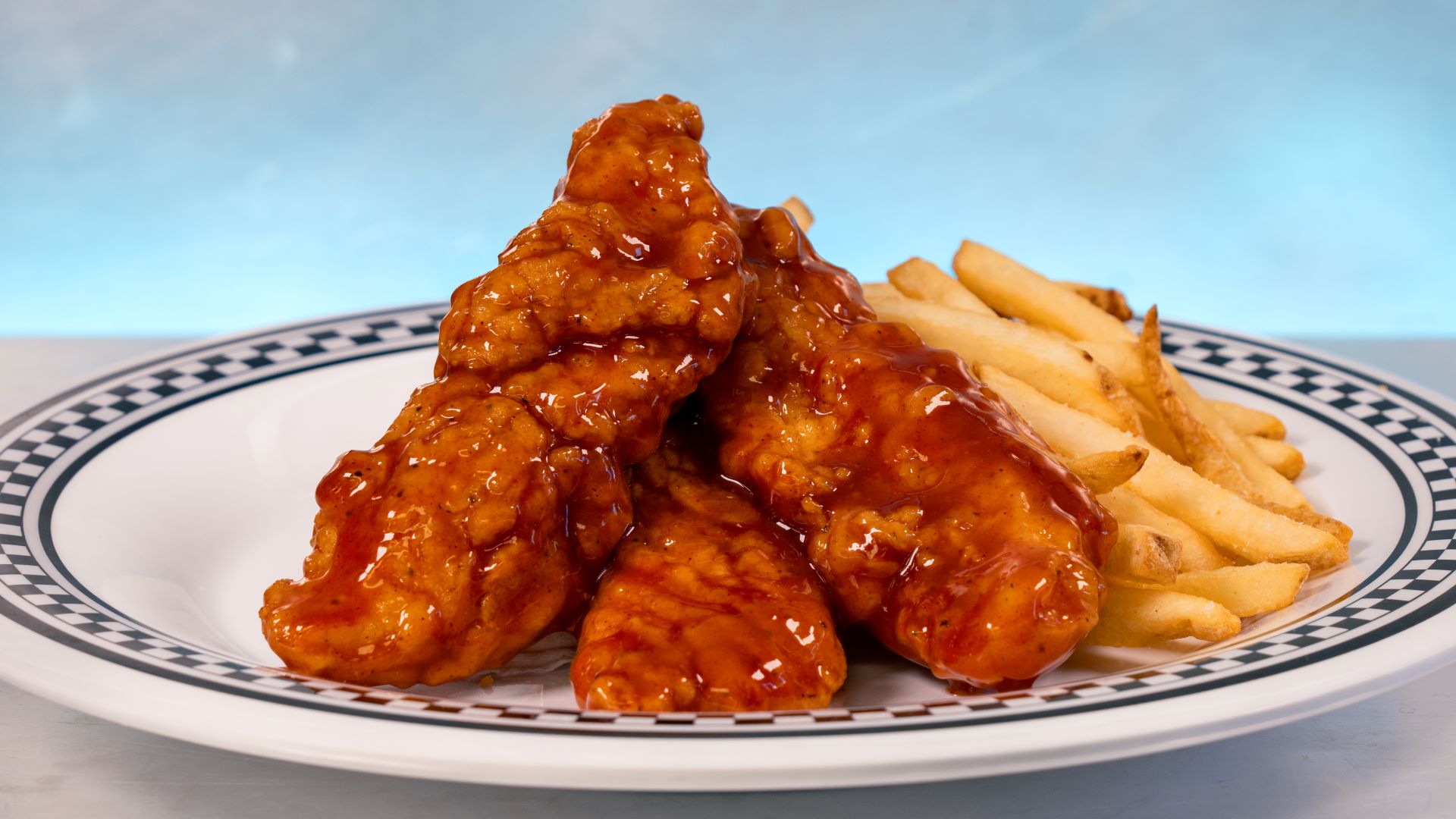 Three chicken tenders in sauce, served with French fries on a plate.
