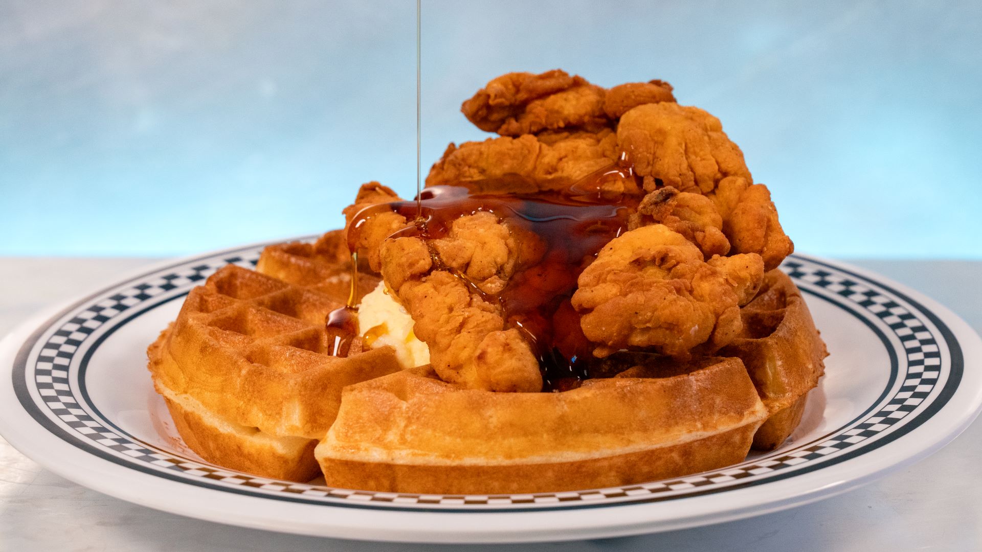 Chicken and waffles drizzled with syrup on a plate.