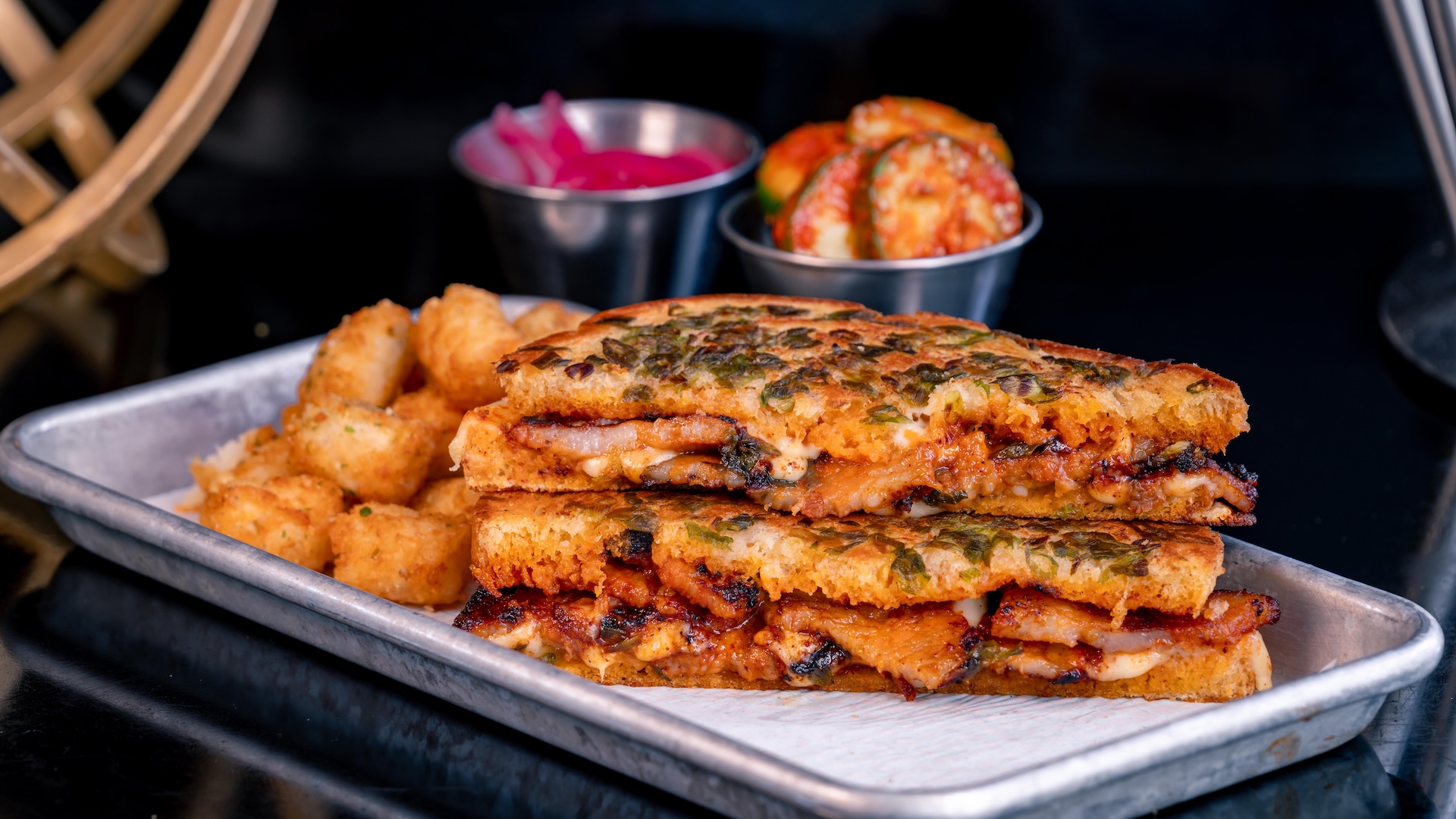 Spicy Pork Belly Grilled Cheese: Pork belly marinated in Korean spices with white American cheese, spicy a&iuml;oli, pickled onions, sourdough bread, and green onion crust served with potato bites (New)