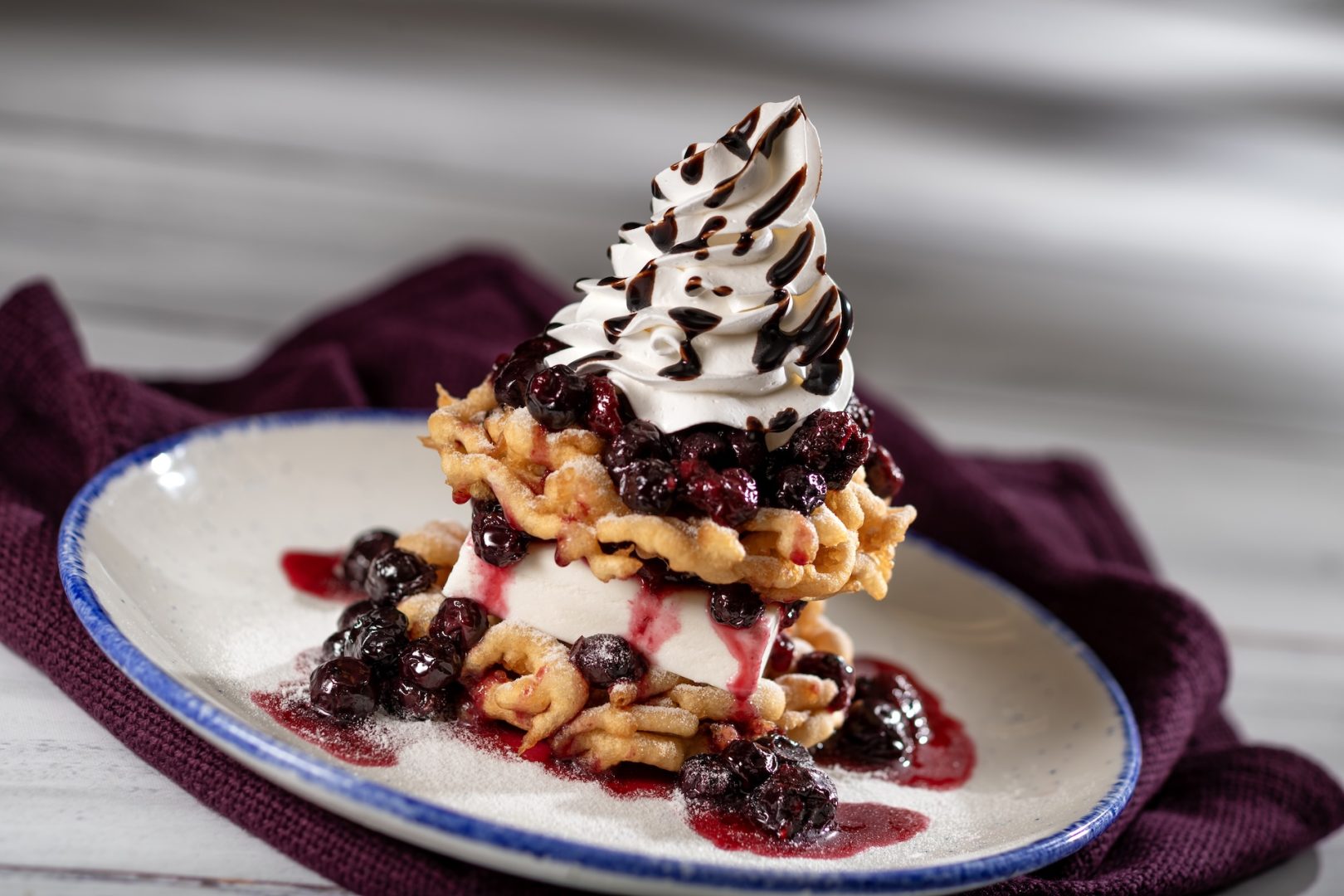Wild Berry Funnel Cake: Funnel cake sandwich with vanilla ice cream and powdered sugar topped with brown sugar brandy-wild berry compote, whipped cream, and dark chocolate sauce (New)