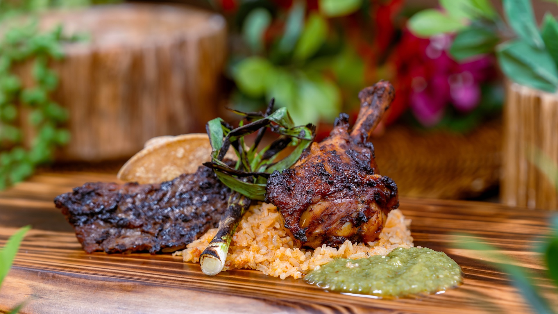 Grilled meat, rice, and green sauce on a wooden platter with garnishes.