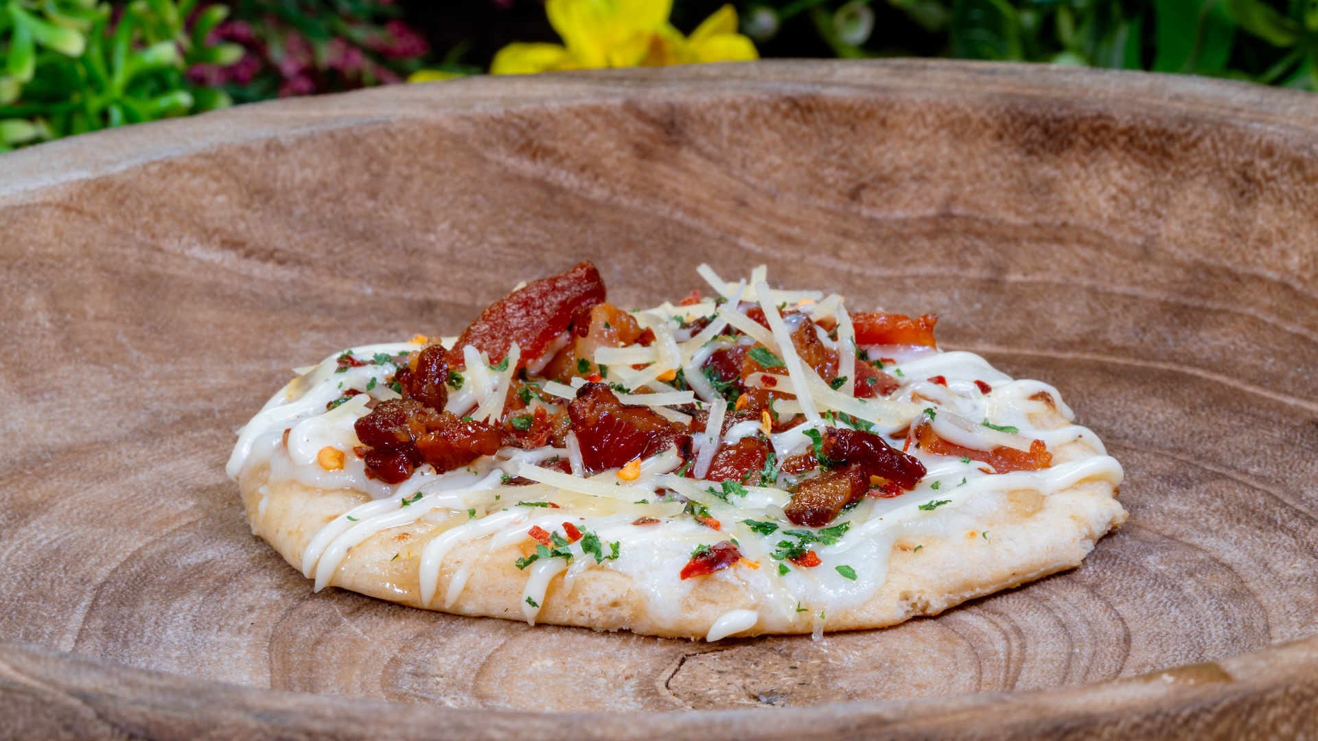 Pizzetta topped with bacon, cheese, and herbs on a wooden plate.