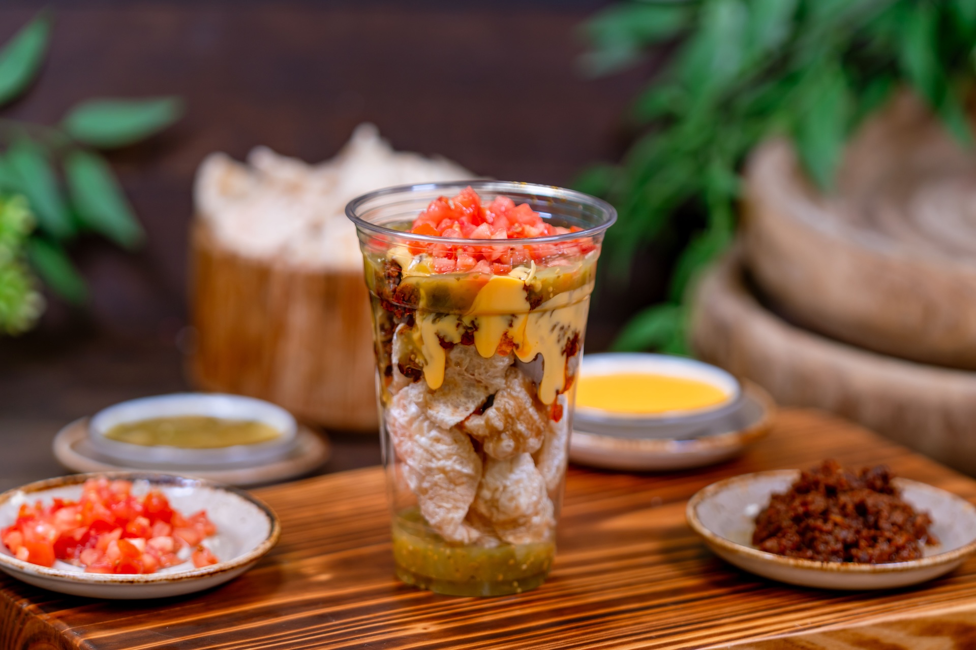 Chicharron nachos in a cup, topped with cheese and tomatoes.
