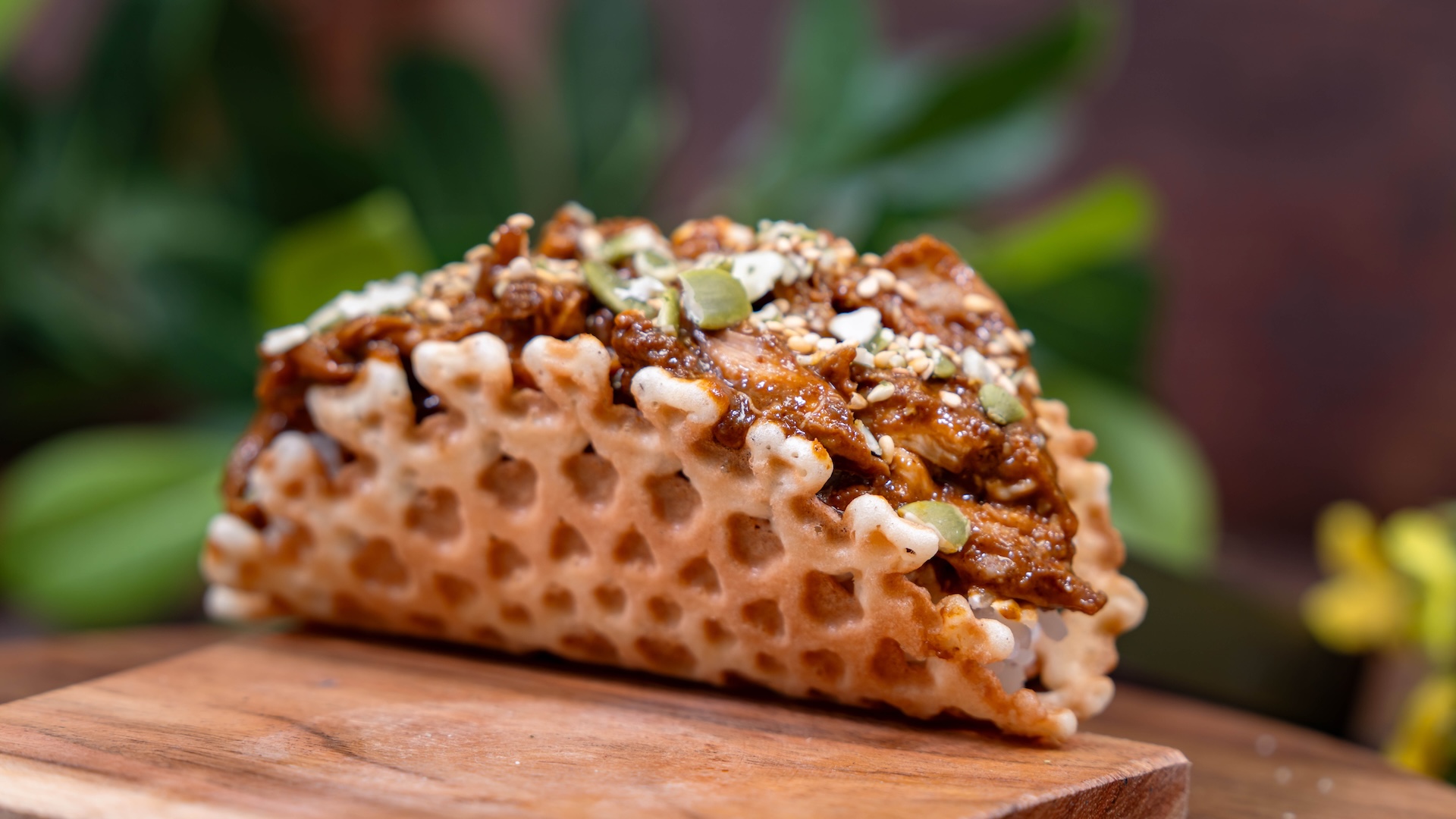 Waffle taco filled with chicken, topped with seeds and herbs.