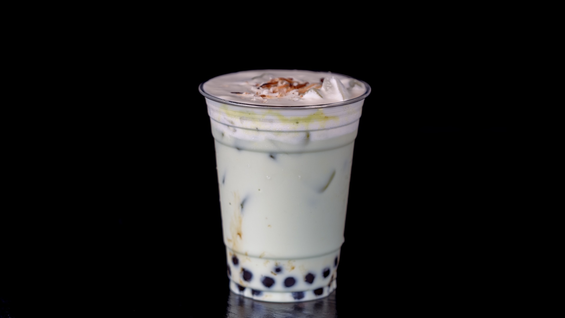 Iced pandan milk tea with toppings in a clear cup against a black background.