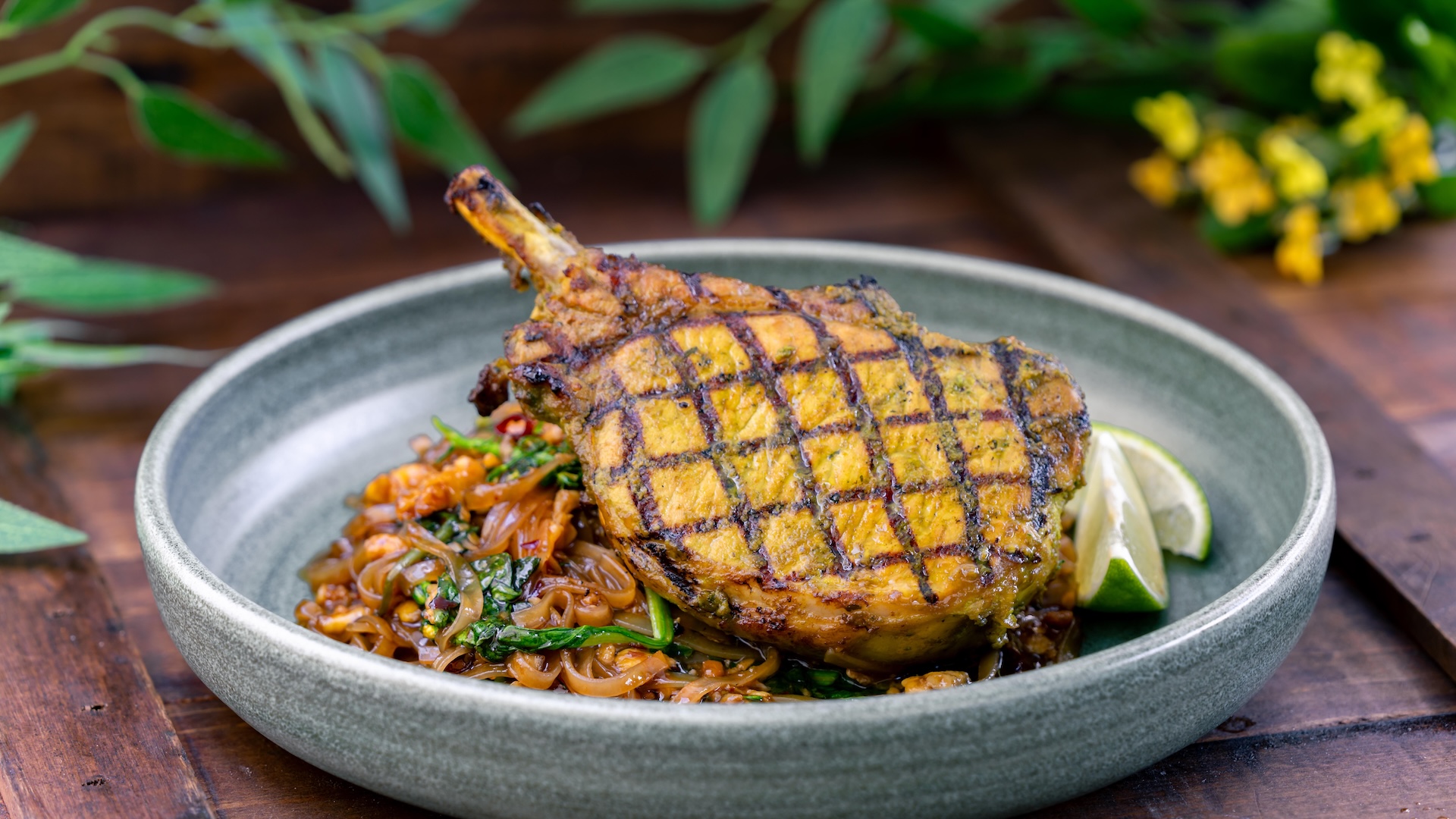Grilled pork chop served over noodles with lime wedges.