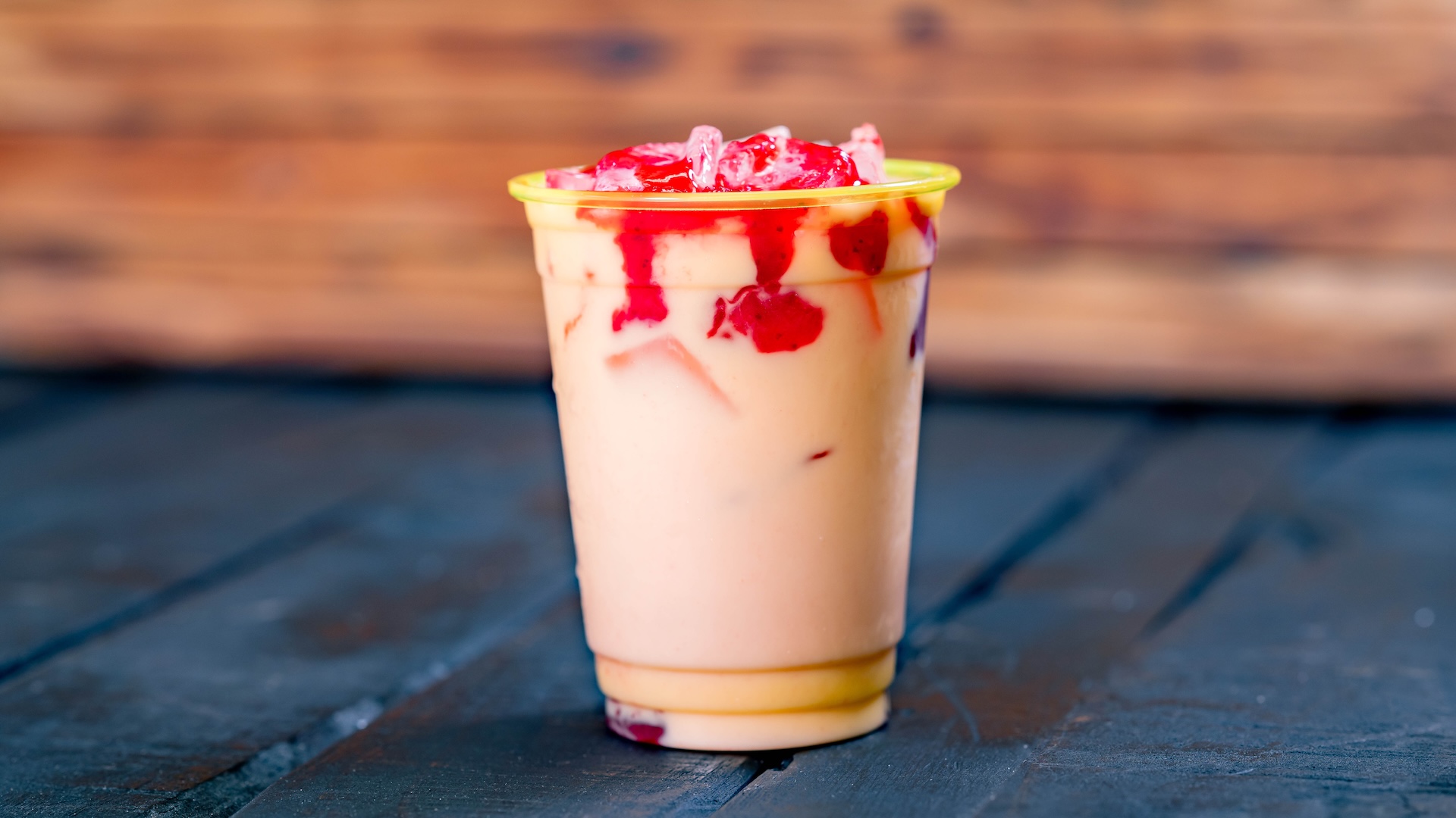 Strawberry horchata drink topped with red syrup in a plastic cup.