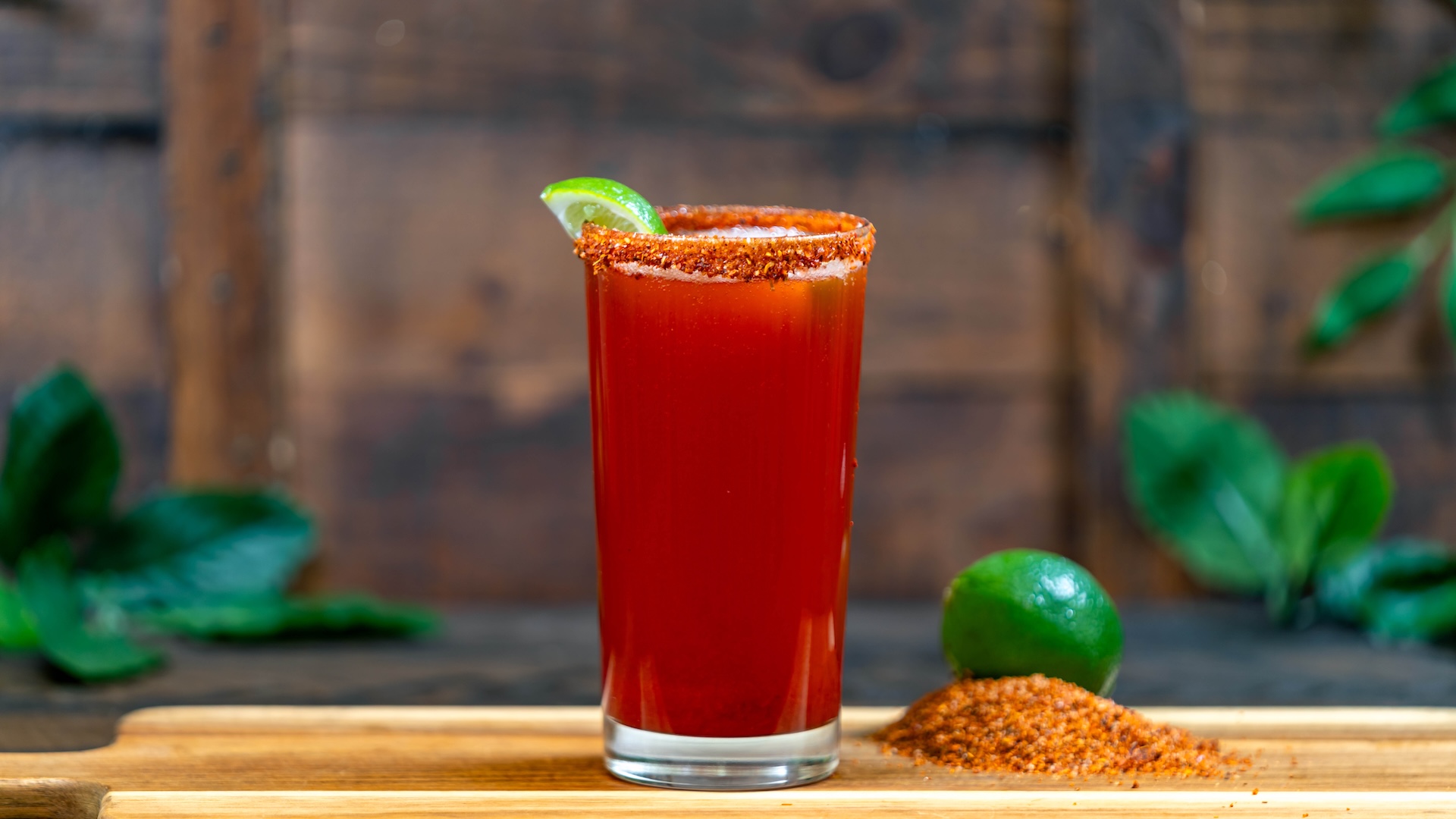 A glass of tropical michelada garnished with lime and chili salt.