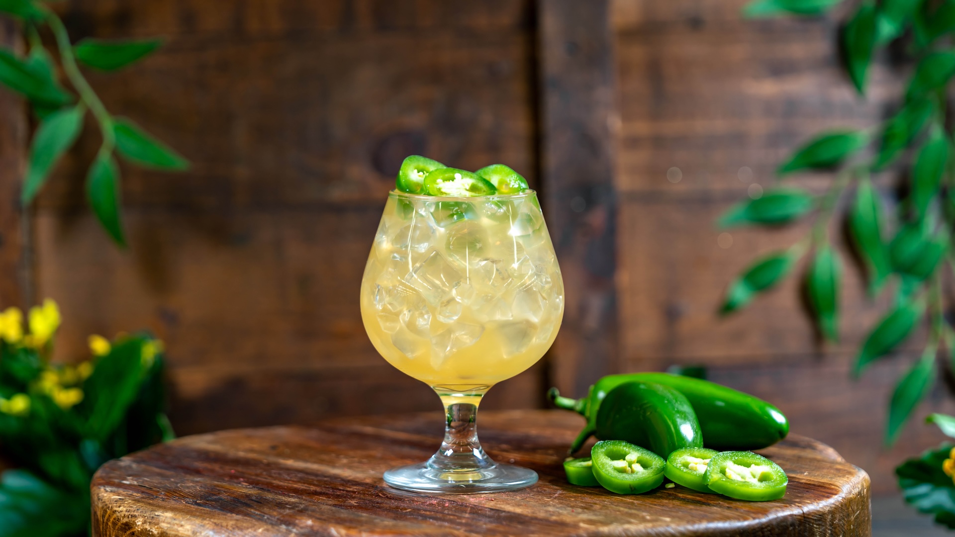 Cocktail glass with jalapeños on ice, wooden table background.