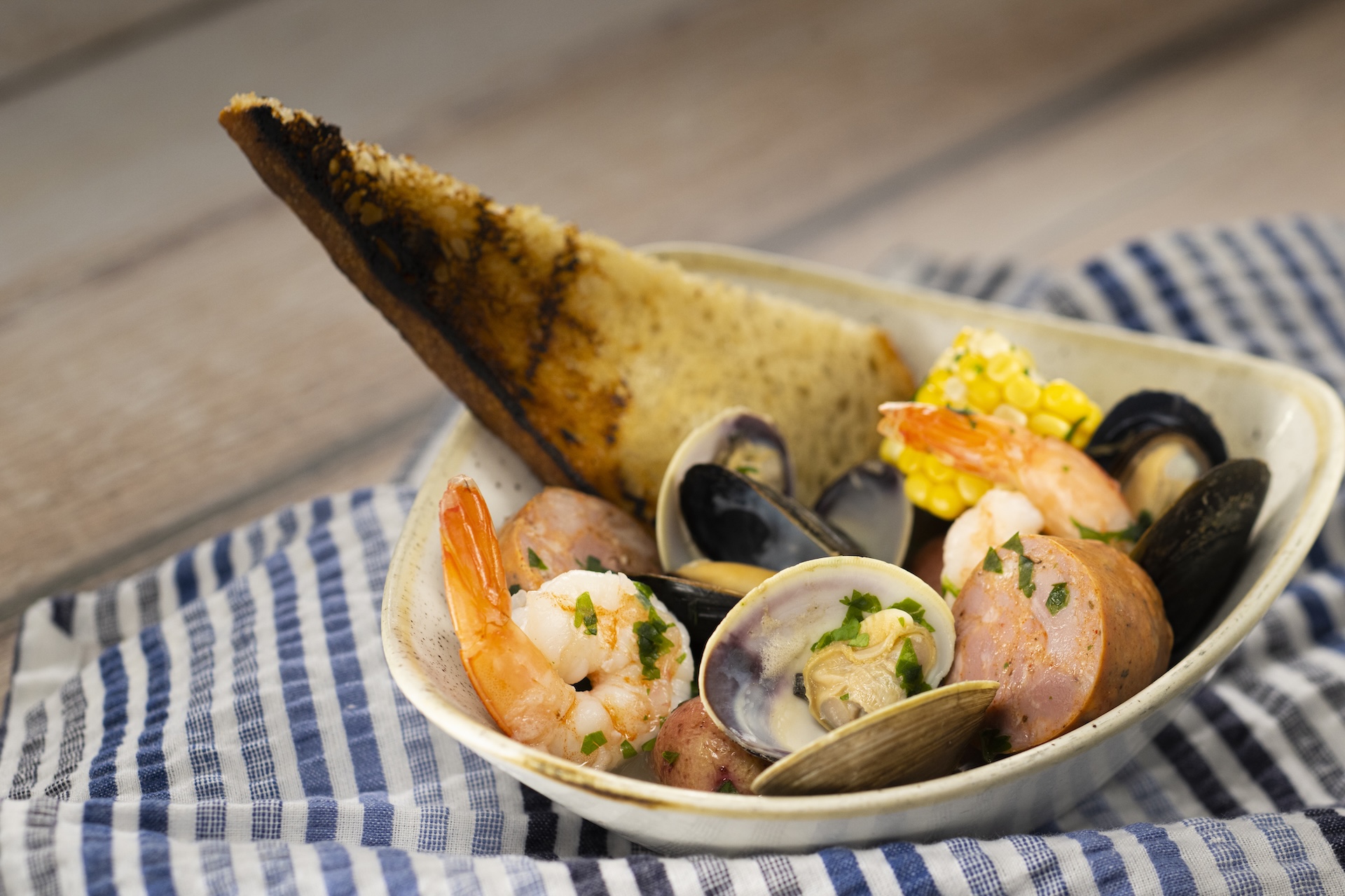 Seafood Bake with shrimp, mussels, clams, andouille sausage, red potatoes, corn on the cob, persillade butter, white wine broth, and grilled sourdough