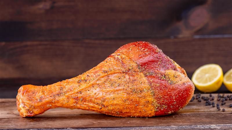Lemon pepper turkey leg on a wooden surface, garnished with lemon slices.